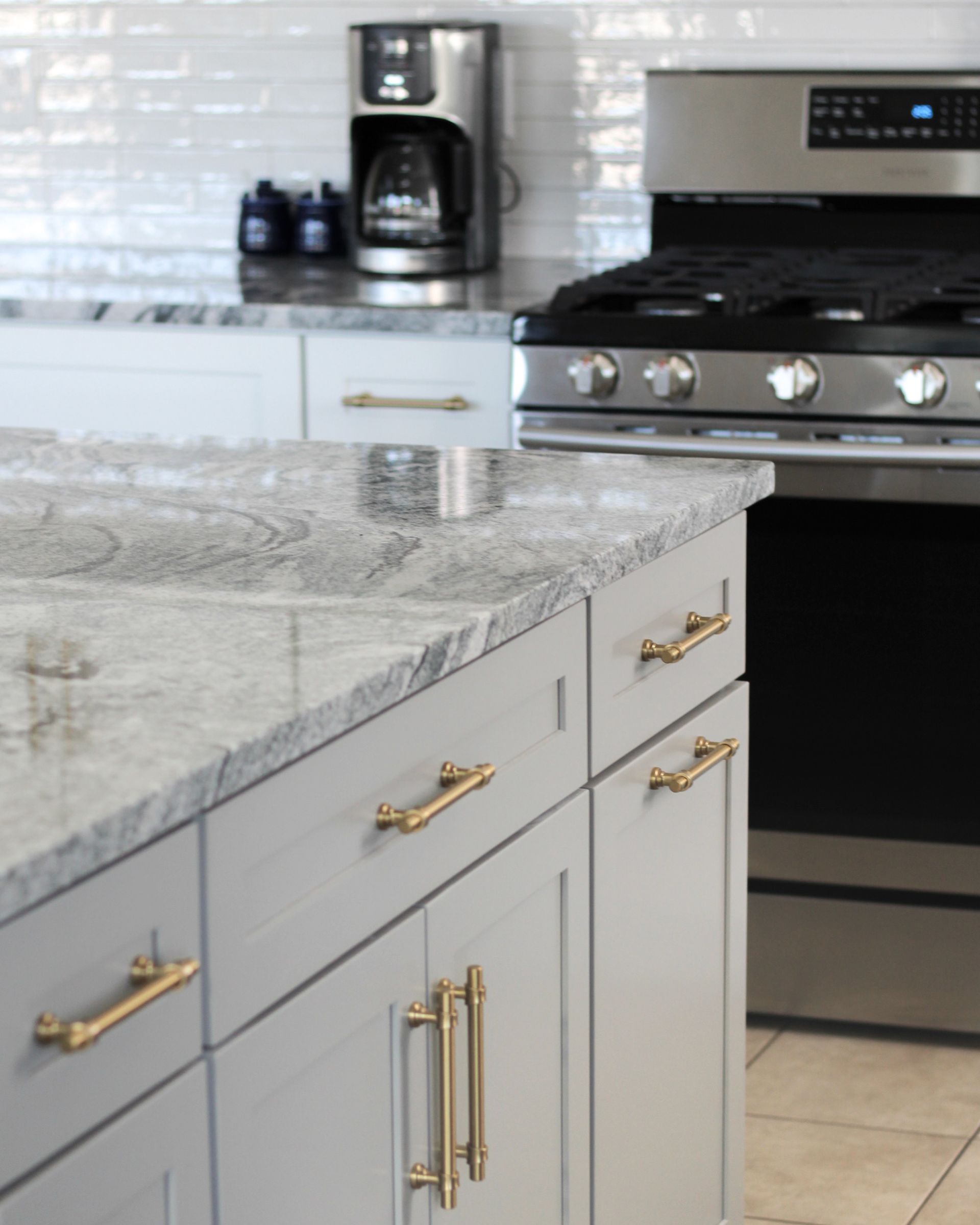 Modern kitchen with gray cabinets, granite countertop, stainless steel stove, and coffee maker