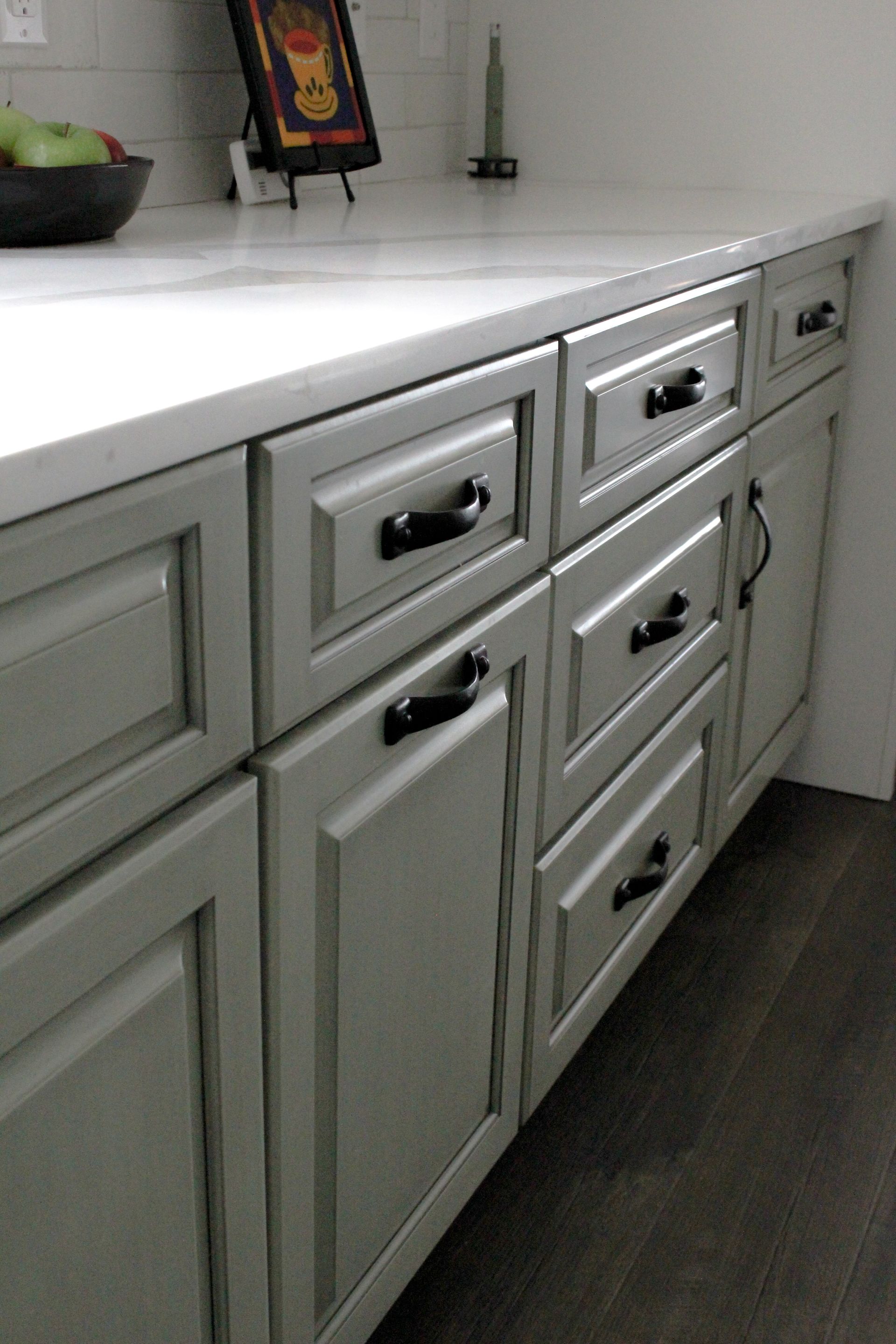 White kitchen cabinets with black handles and a gray countertop, shown along a corner wall.