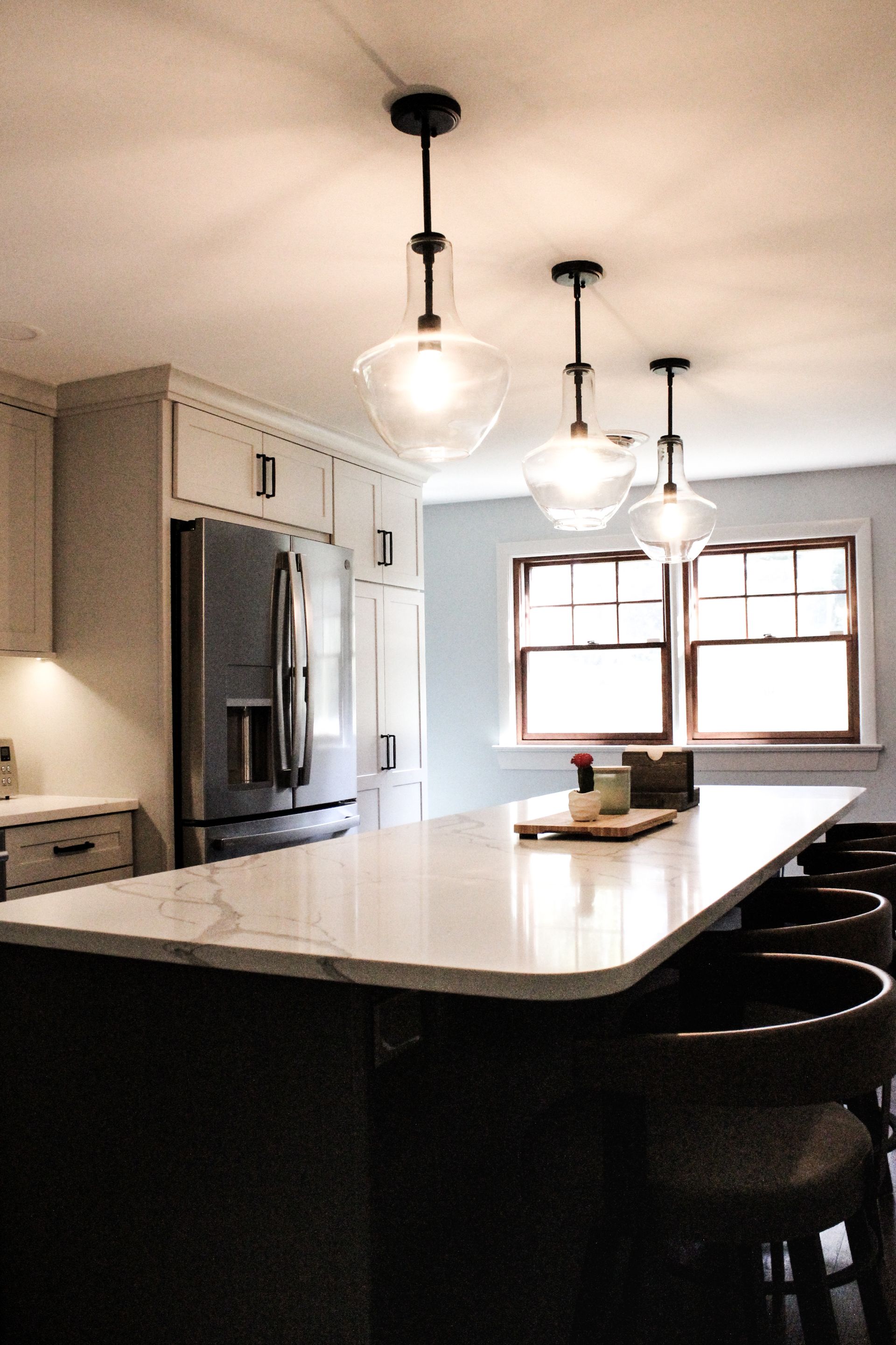 Modern kitchen with white island, pendant lights, stainless fridge, and two windows