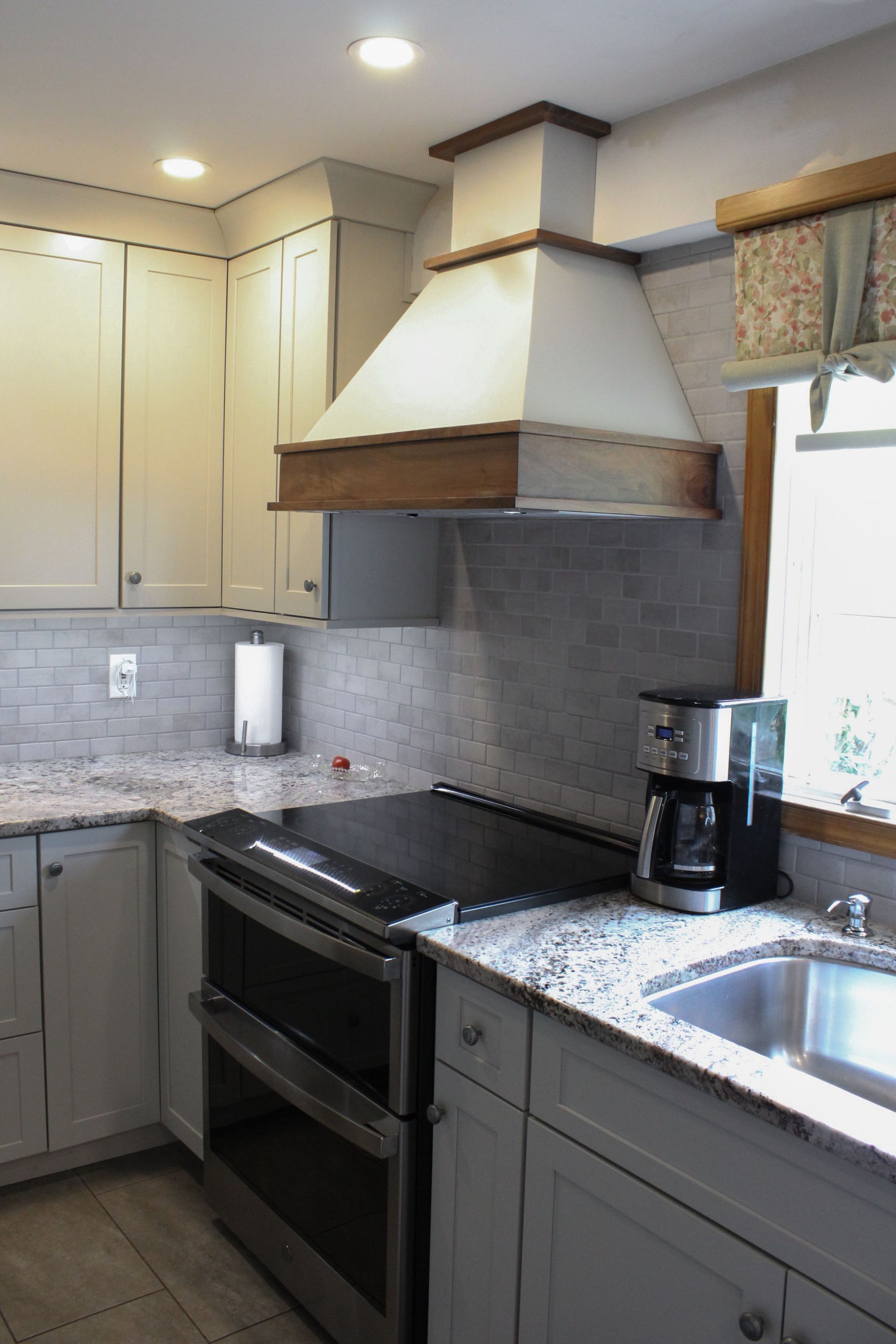 Modern kitchen with gray cabinets, black stove, white range hood, granite counters, and a sink by the window