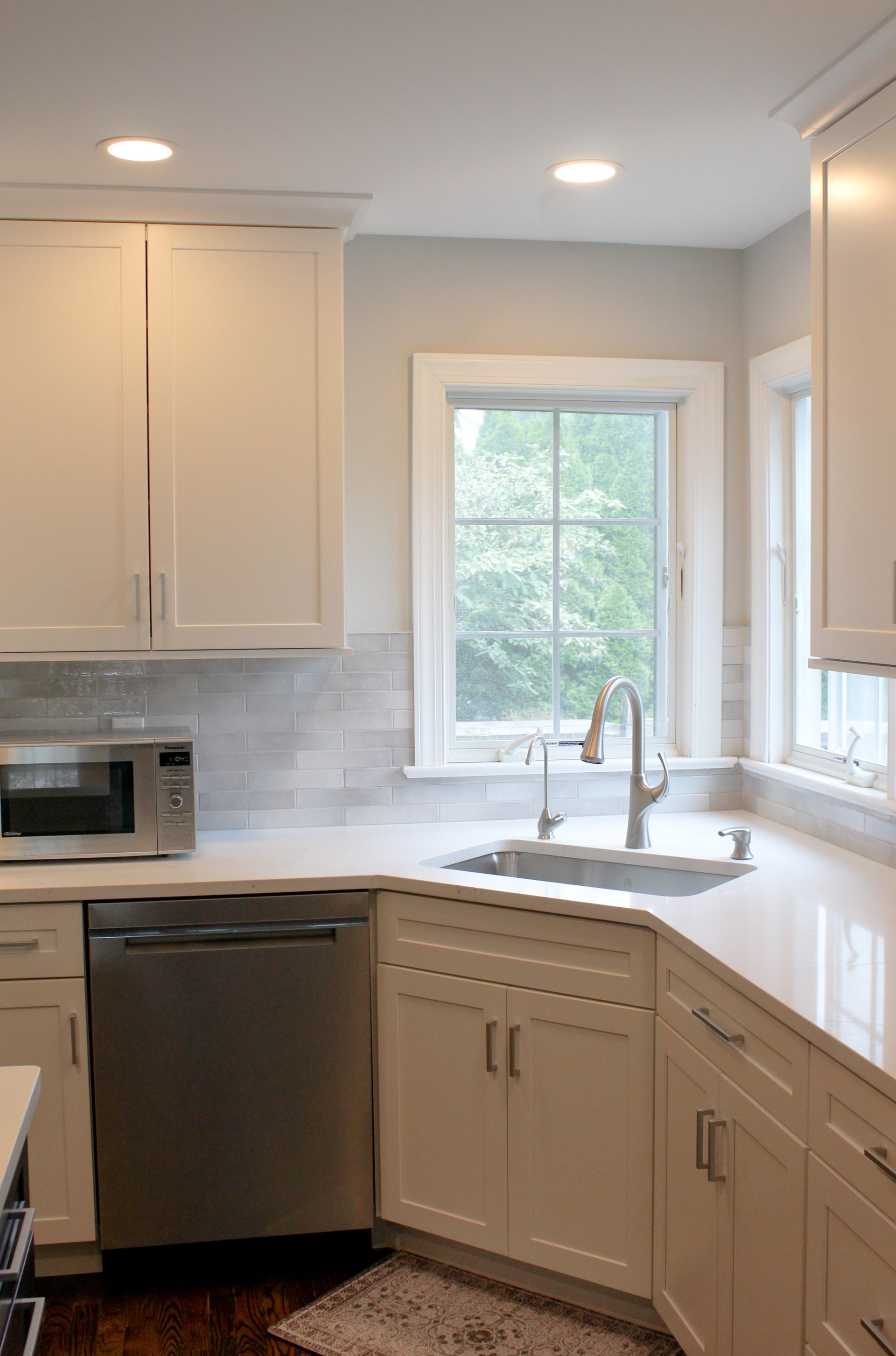 Bright modern kitchen with white cabinets, gray tile backsplash, stainless dishwasher, and a window over the sink.