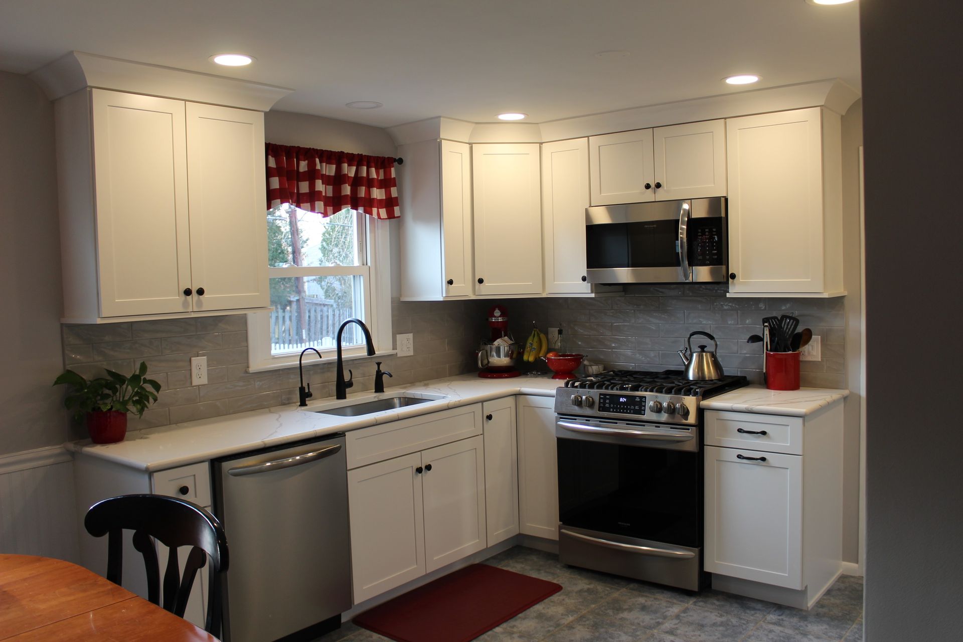Bright white kitchen with stainless steel stove, sink, and cabinets, red accents, and a window over the sink