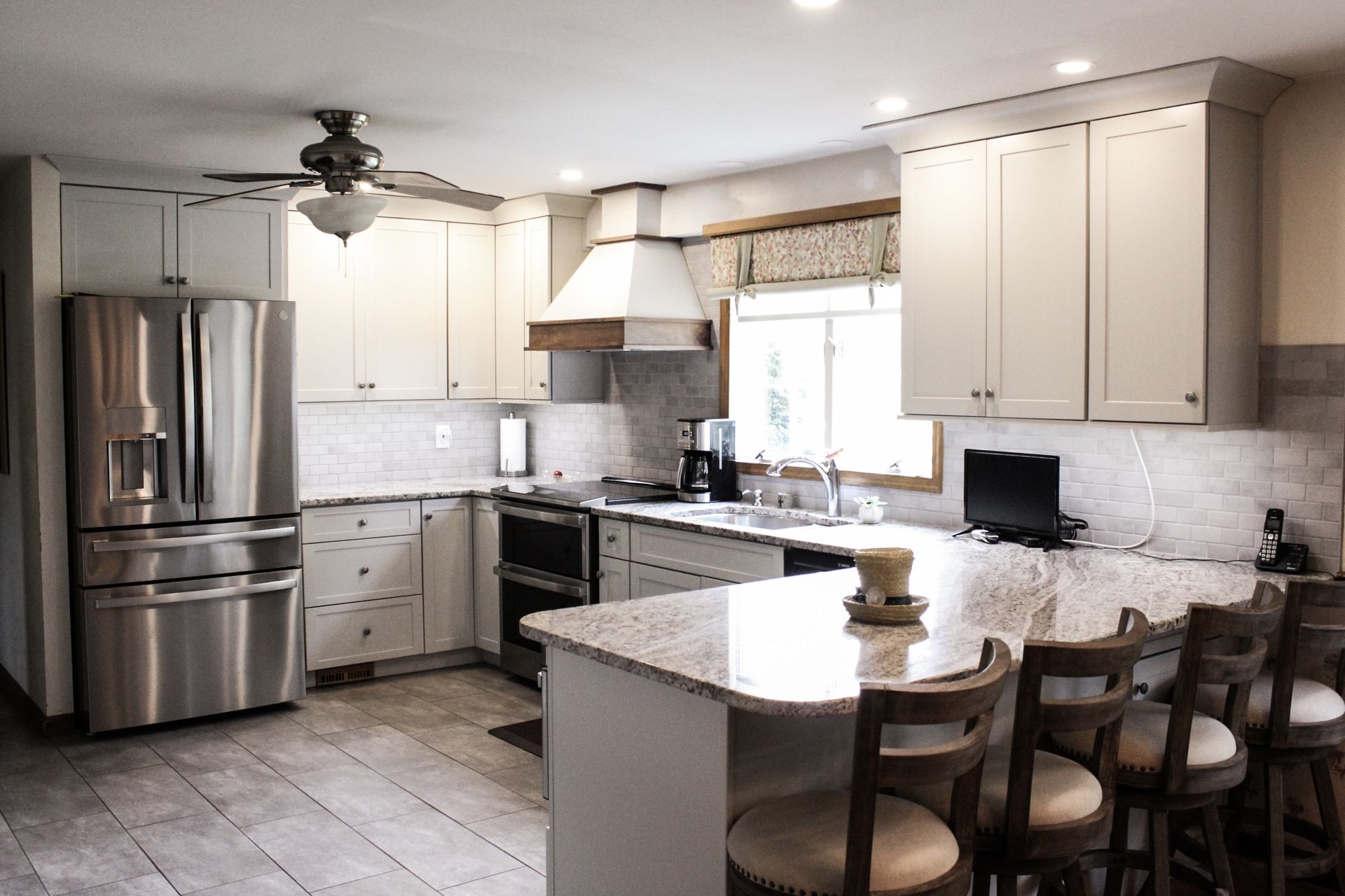 Bright modern kitchen with stainless steel appliances, white cabinets, and a breakfast bar with stools.