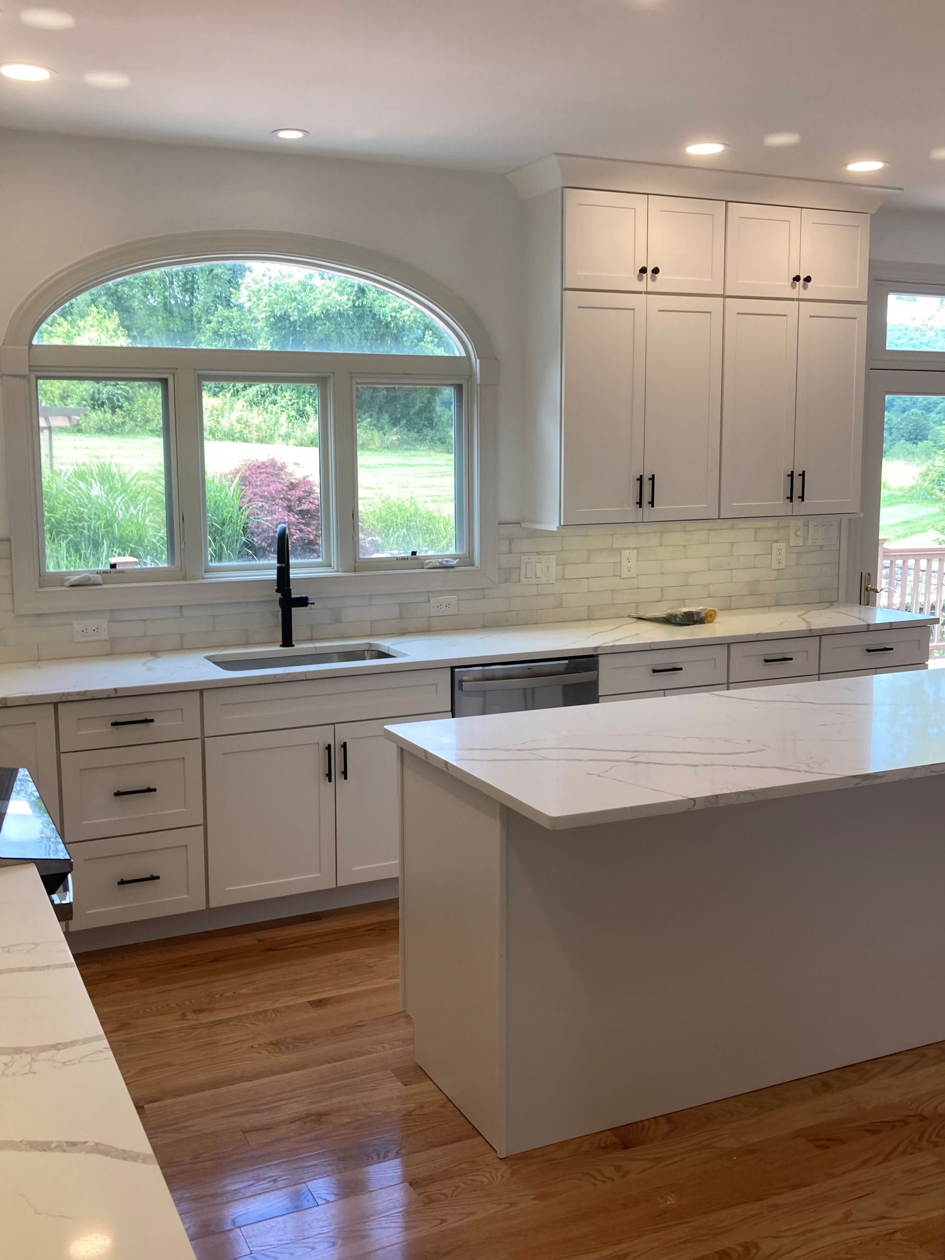Bright white kitchen with a large window, island, and marble countertops, showing a clean modern interior.