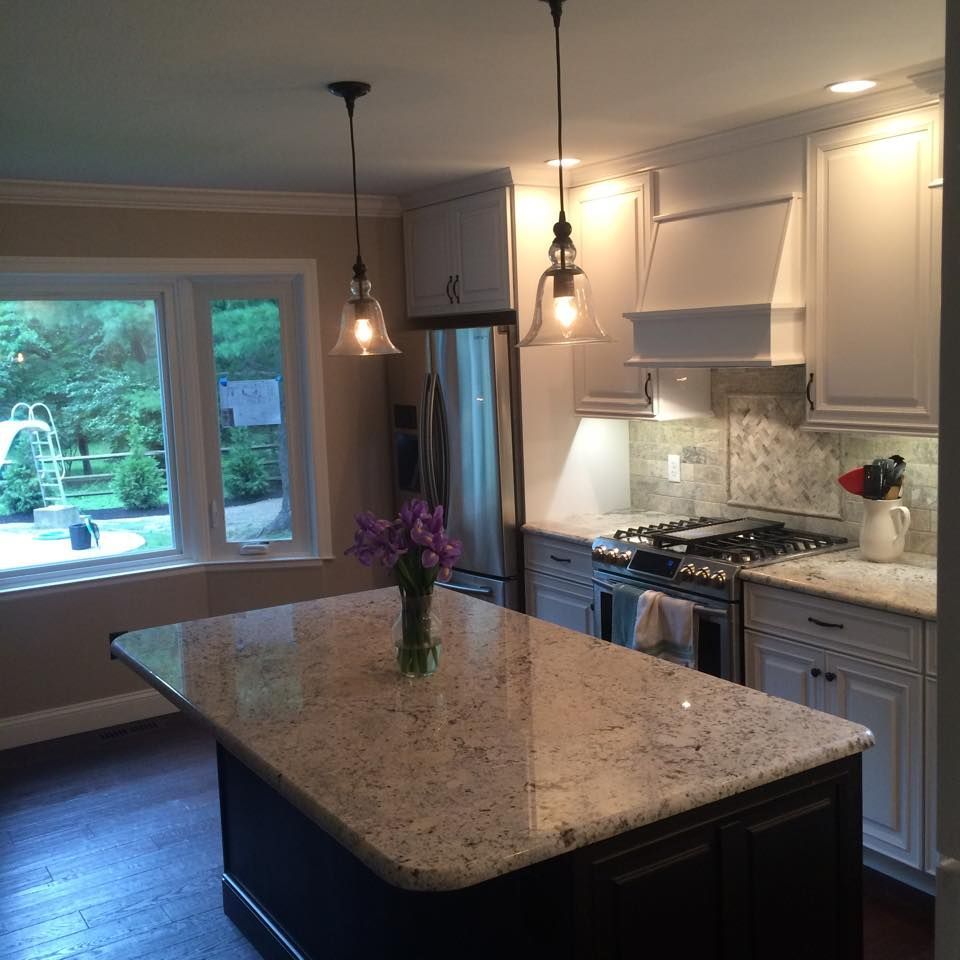 Bright modern kitchen with white cabinets, granite island, pendant lights, and a vase of flowers by the window