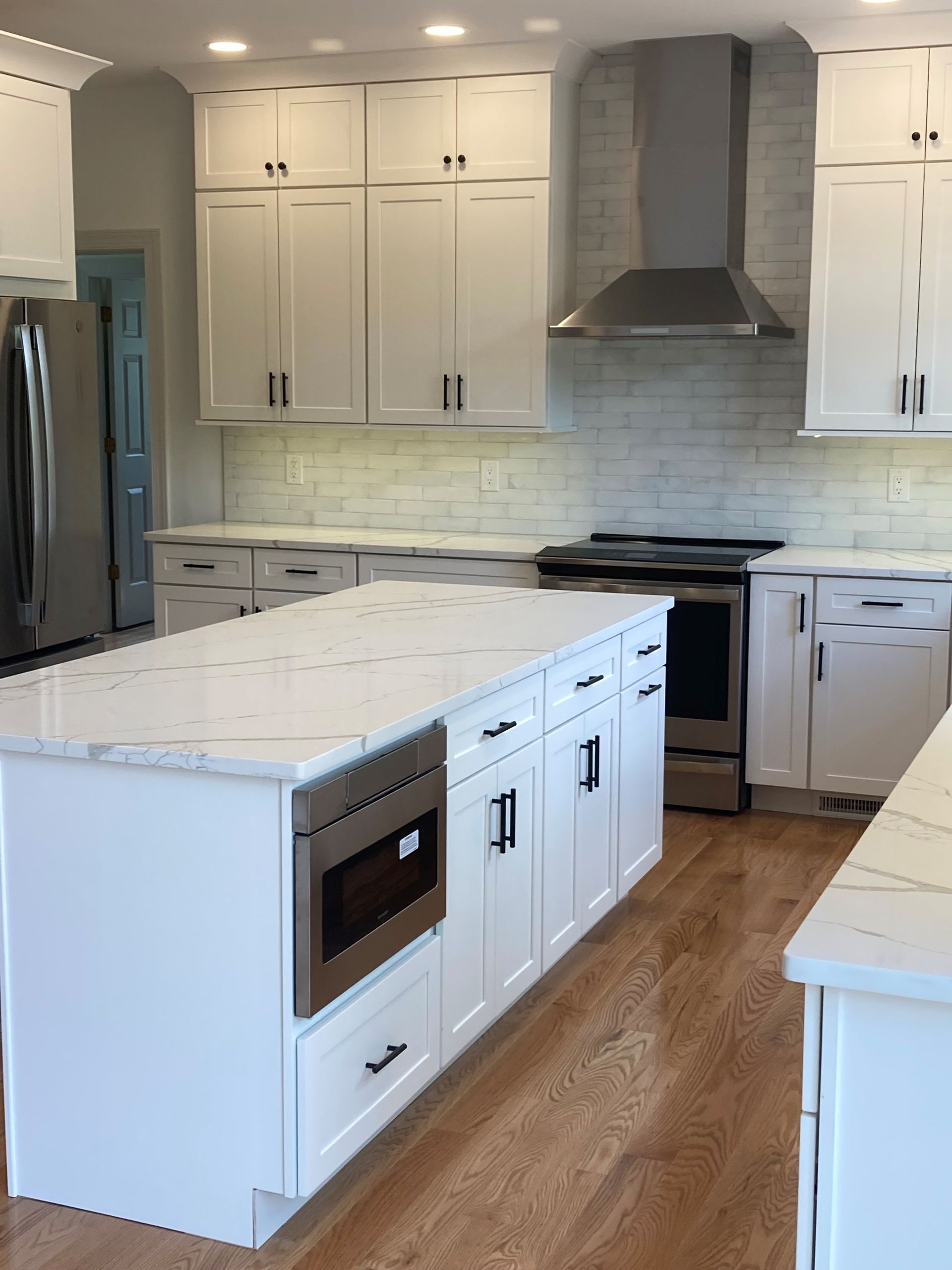 Bright white modern kitchen with island, stainless appliances, and wood flooring.