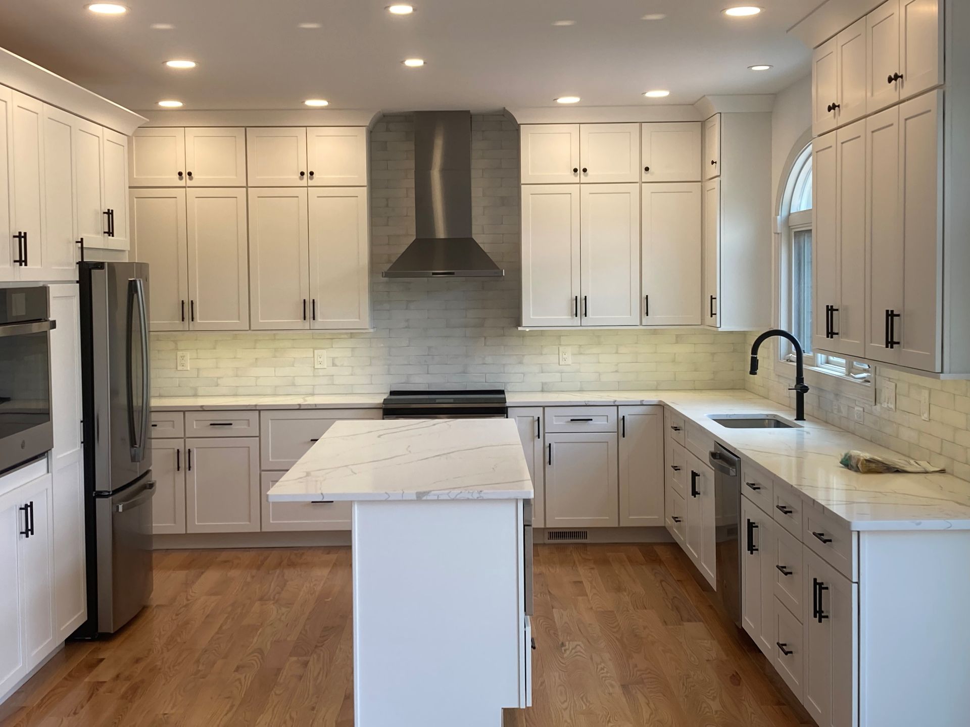 Bright modern kitchen with white cabinets, stainless appliances, wood floor, and central island