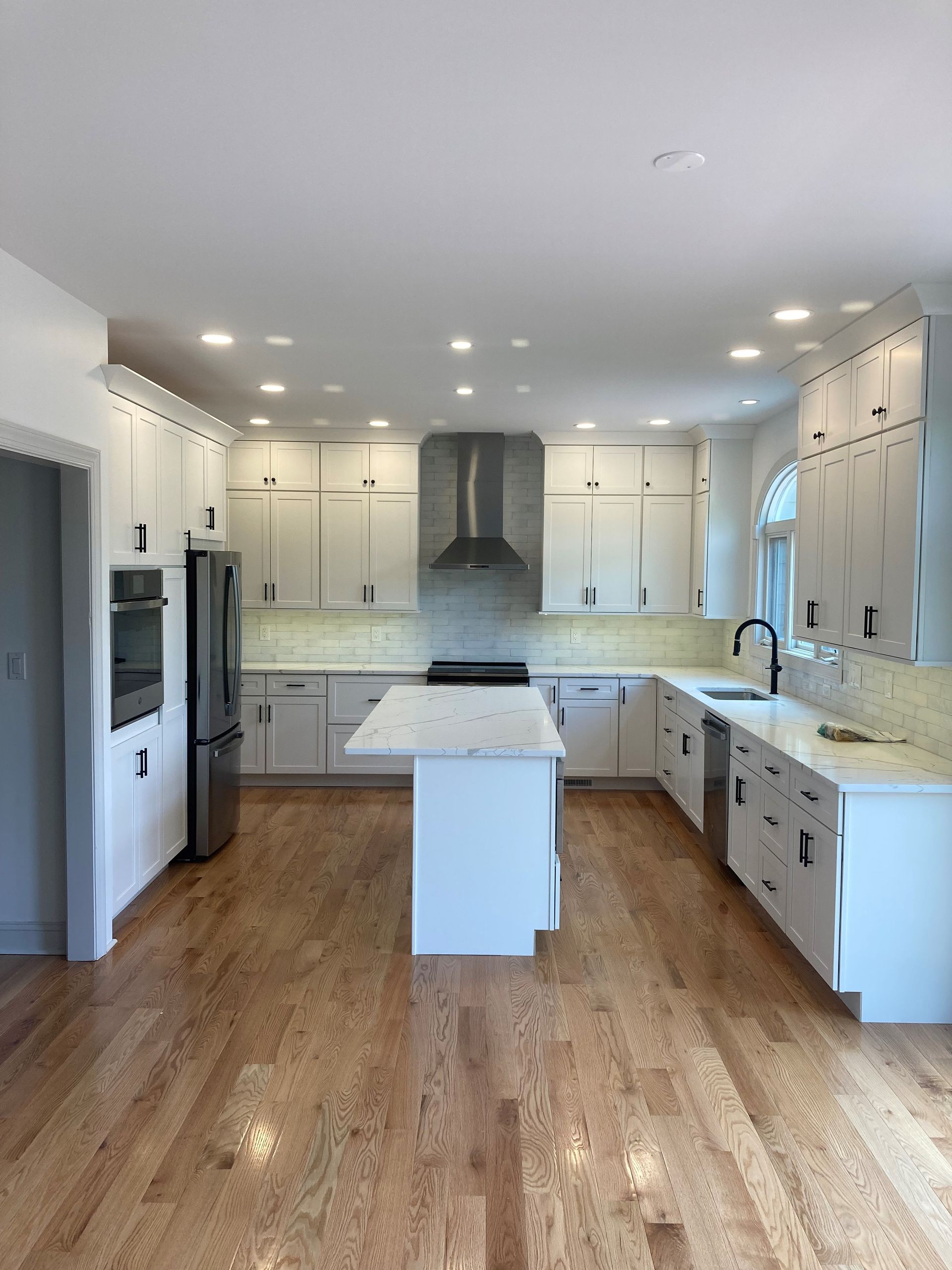 Bright white kitchen with island, stainless range hood, and warm wood floors