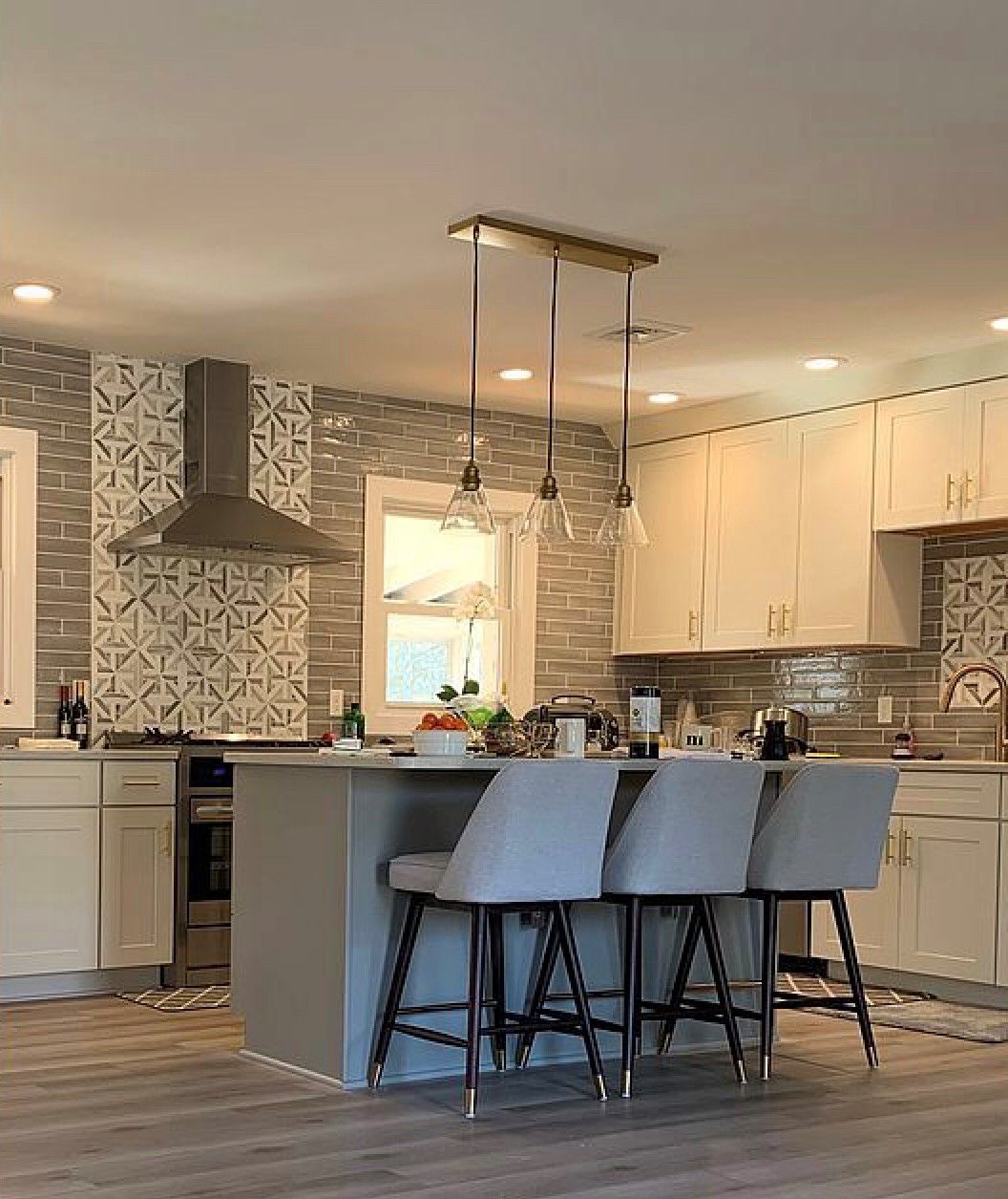 Modern kitchen with island, gray stools, cream cabinets, and stainless steel appliances.