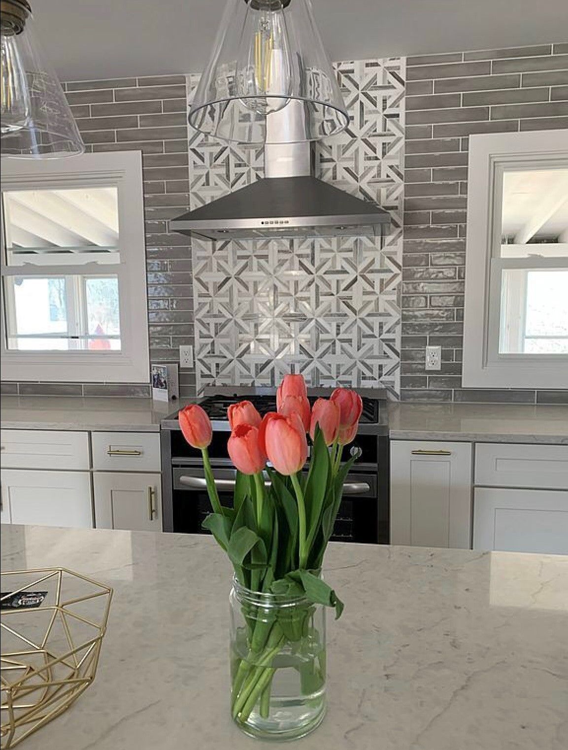 Pink tulips in a glass vase on a kitchen island, with white cabinets and a patterned tile backsplash.