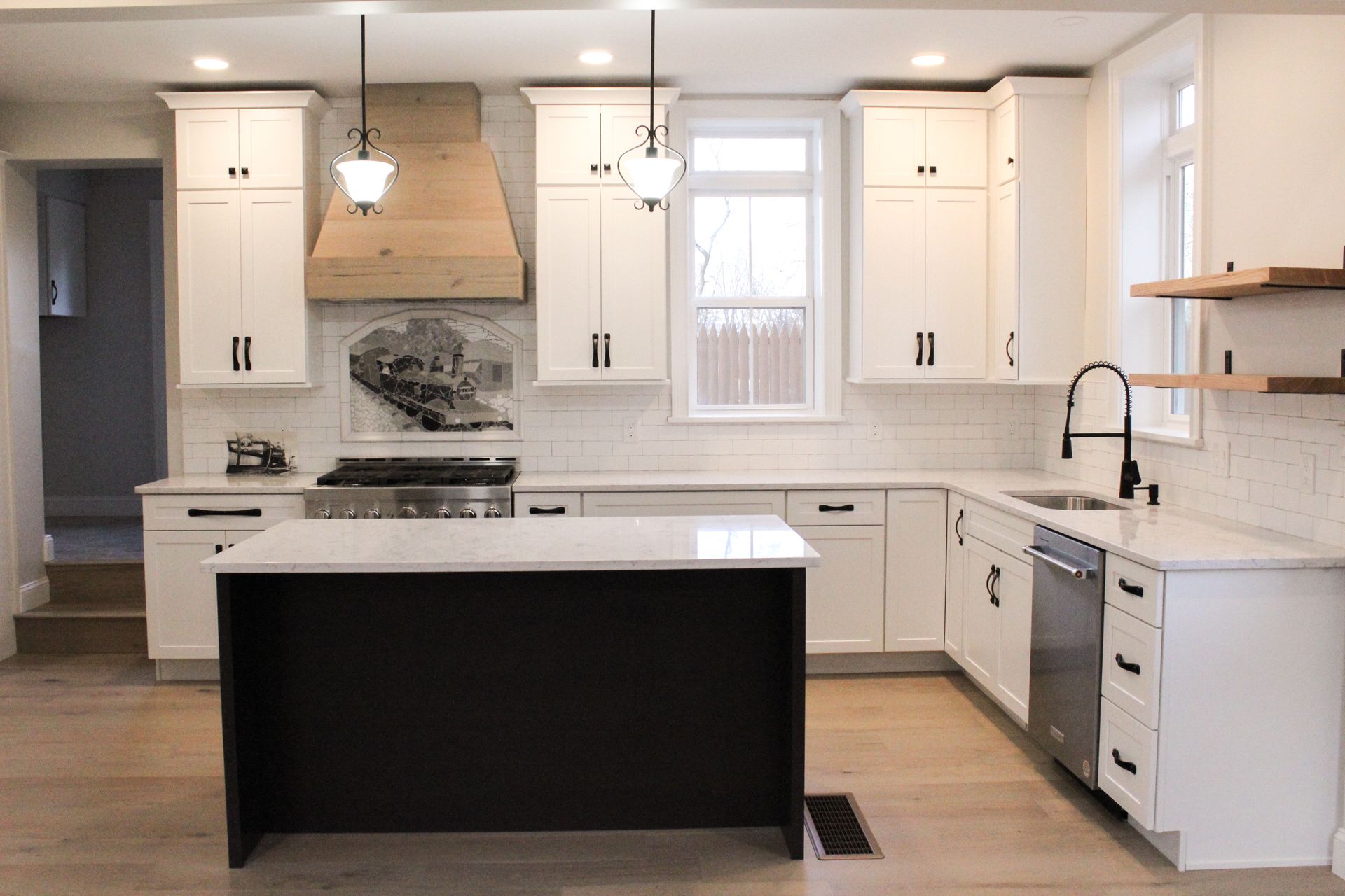 Modern white kitchen with island, pendant lights, wood floors, and stainless-steel appliances