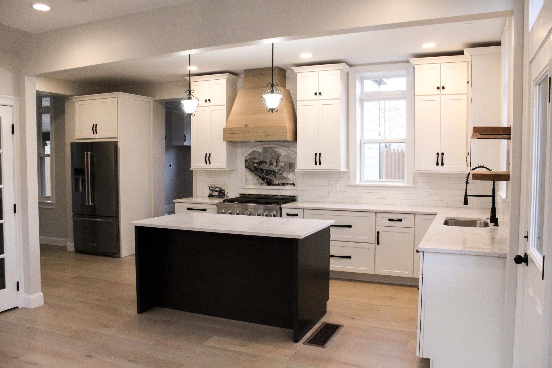 Modern white kitchen with a dark island, stainless appliances, and wood floors