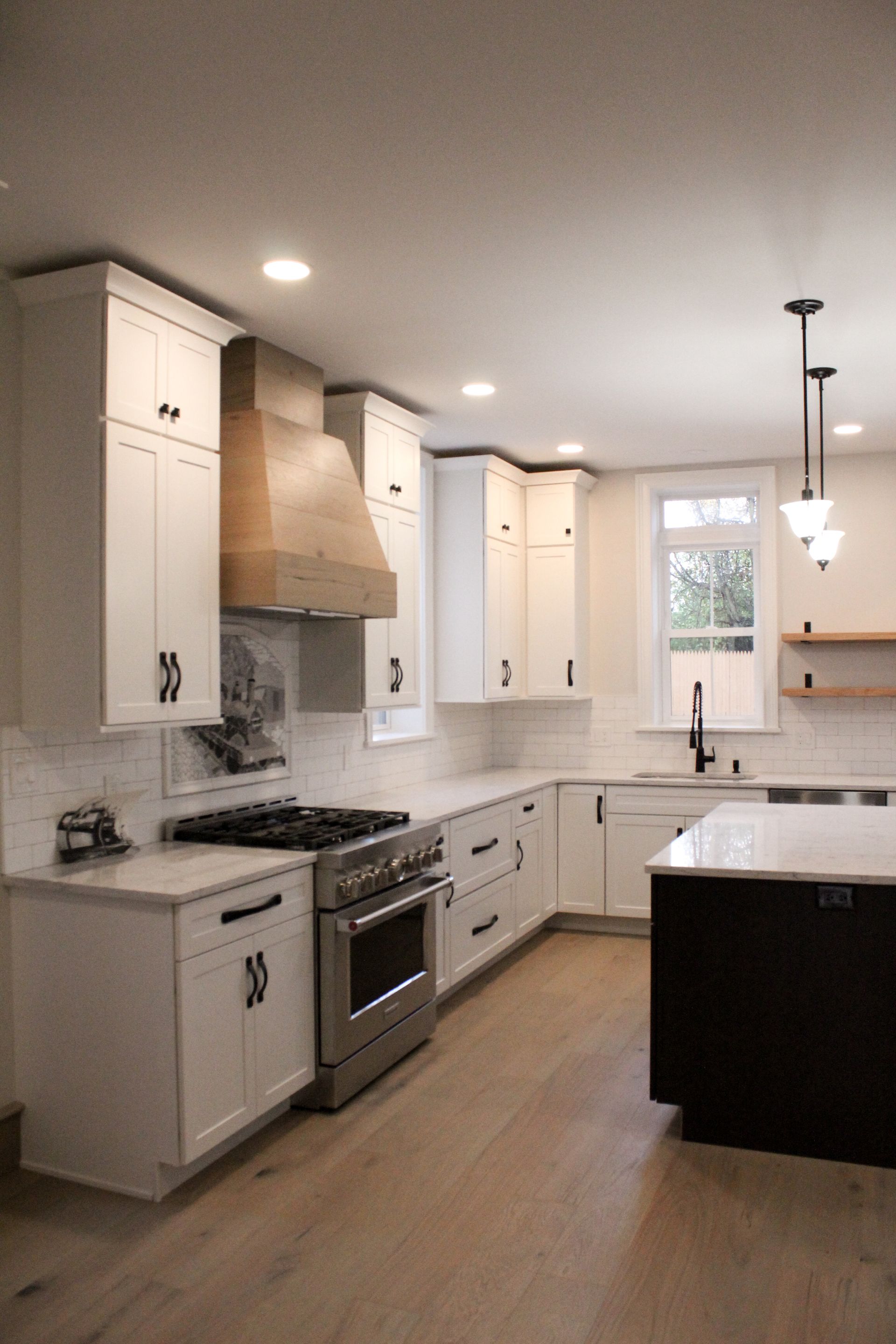 Bright modern kitchen with white cabinets, wood floors, stainless stove, and dark island.
