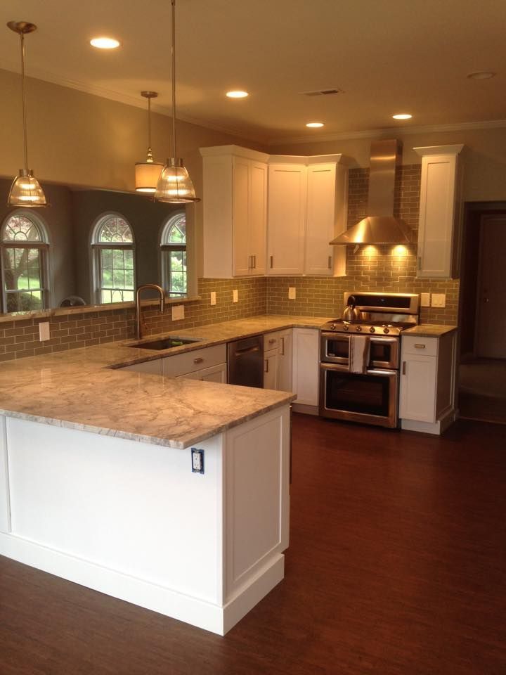Modern kitchen with granite island, white cabinets, stainless stove, pendant lights, and dark wood floors