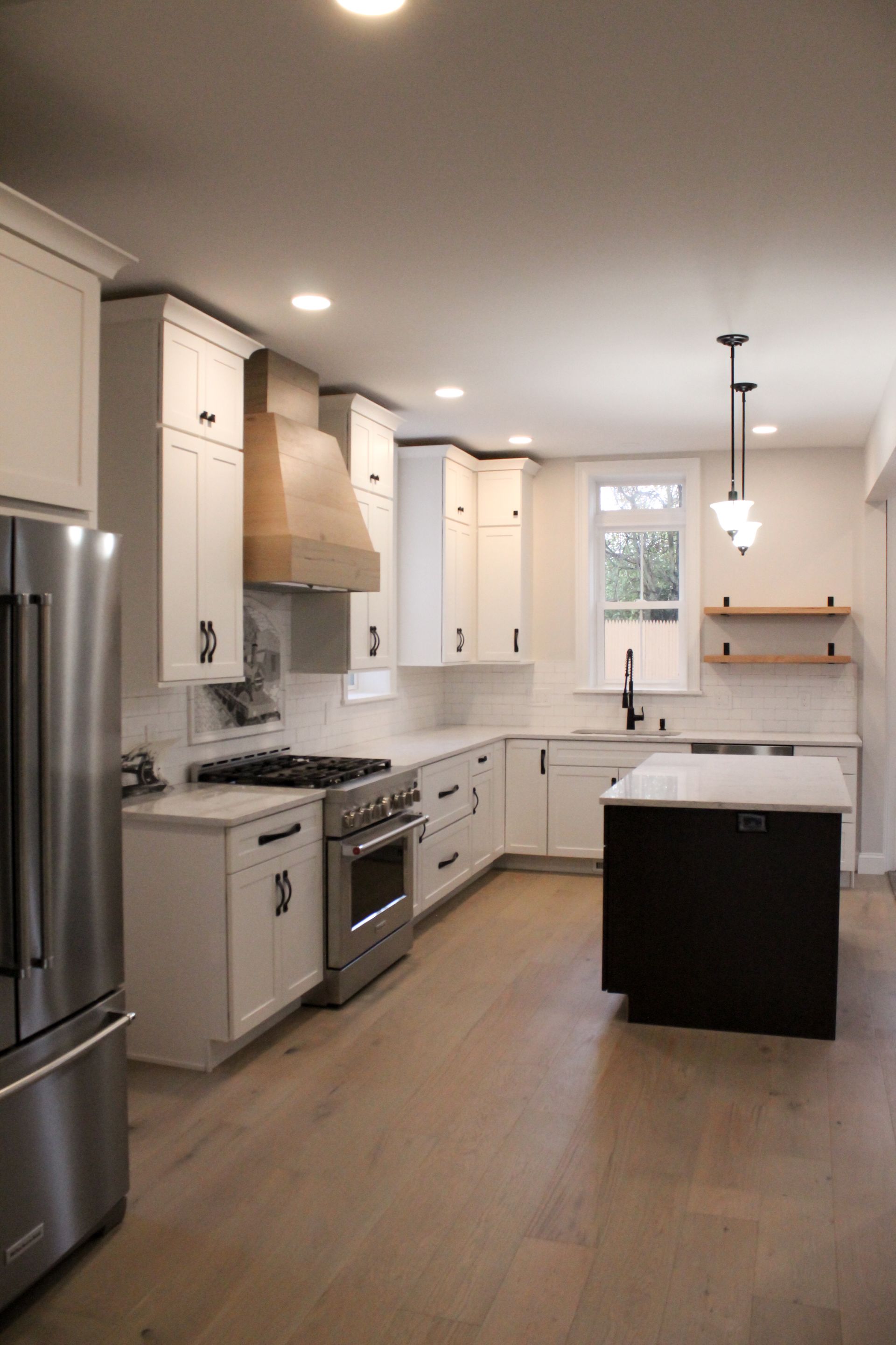 Modern white kitchen with stainless appliances, island, wood flooring, and a window over the sink