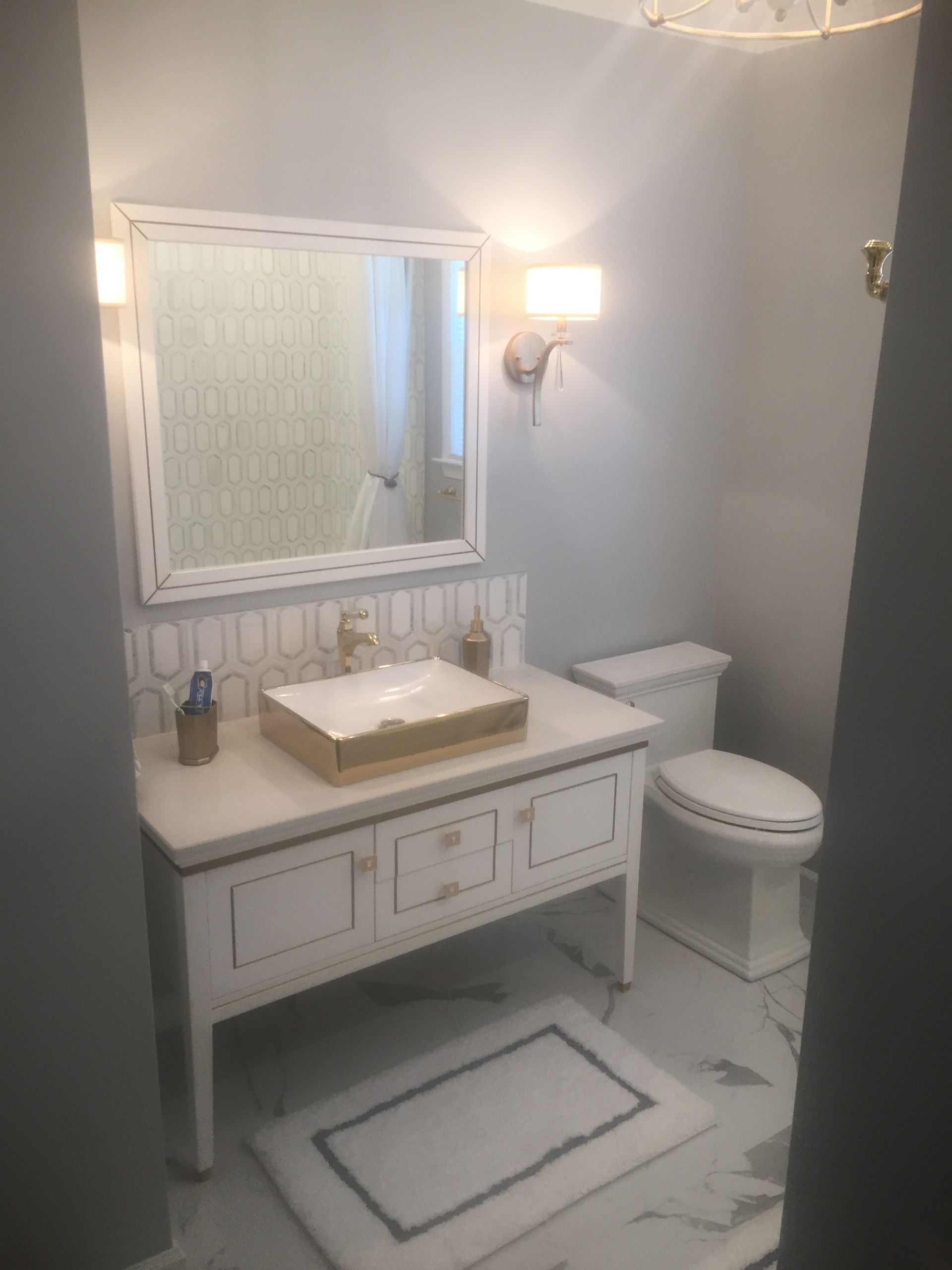 Bright bathroom with white vanity, sink, mirror, toilet, and patterned rug.