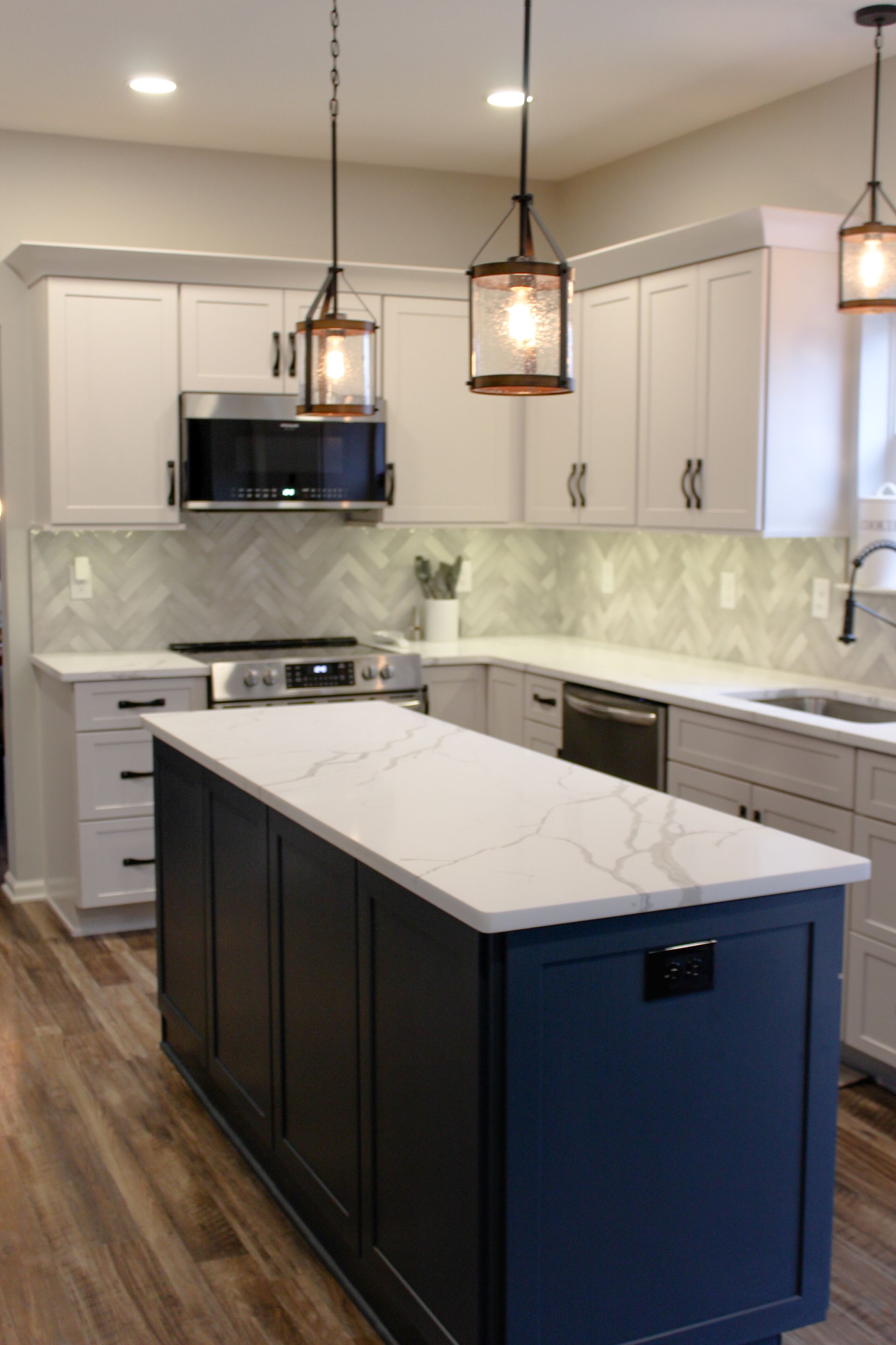 Modern kitchen with dark island, white cabinets, marble backsplash, and hanging pendant lights