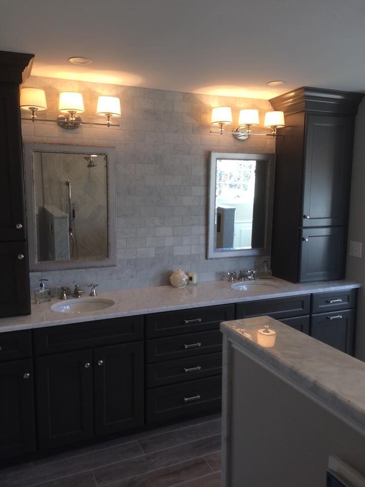 Modern bathroom vanity with dark cabinets, double mirrors, and wall sconces lit above a light countertop
