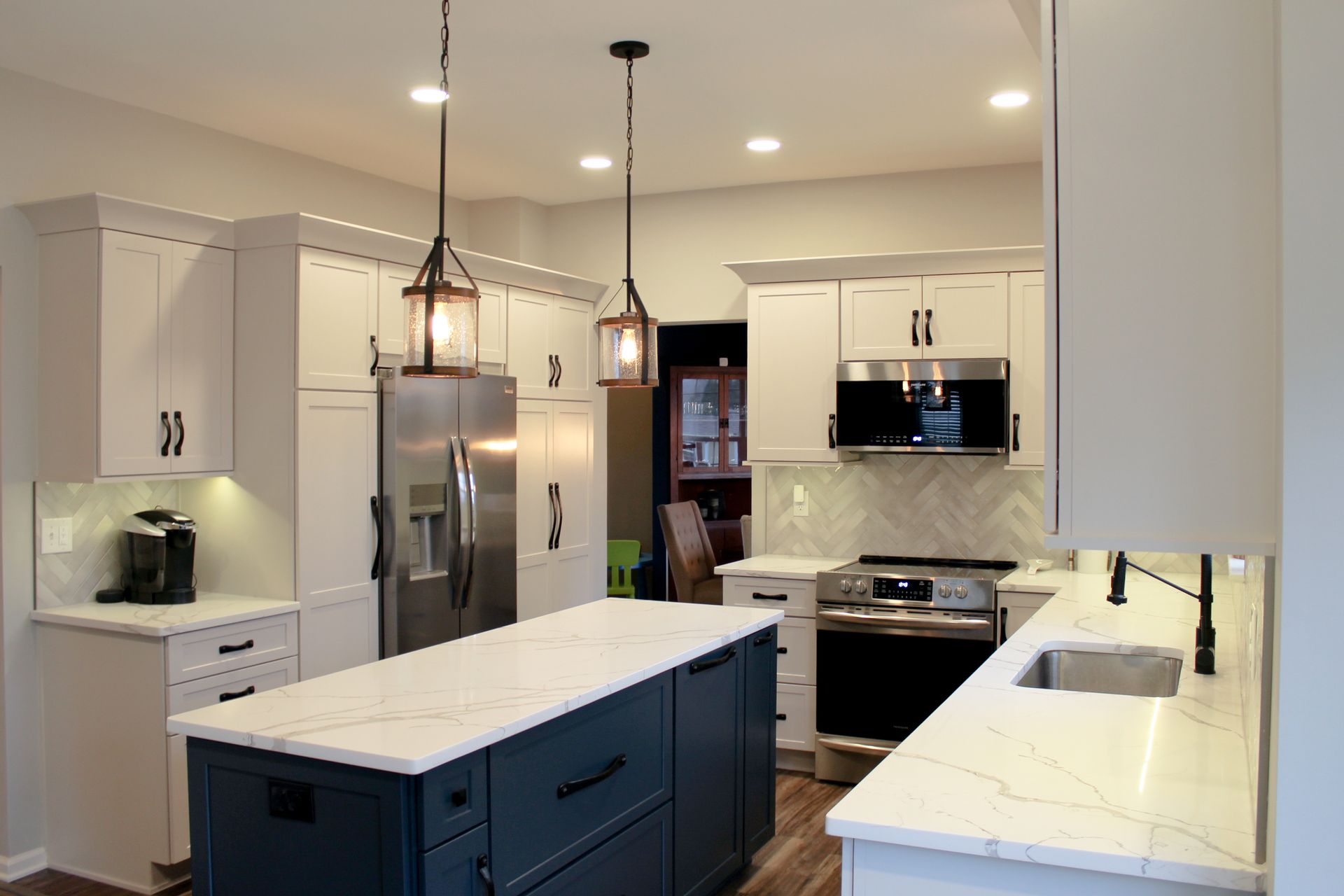 Modern white kitchen with island, stainless-steel appliances, pendant lights, and dark wood floors