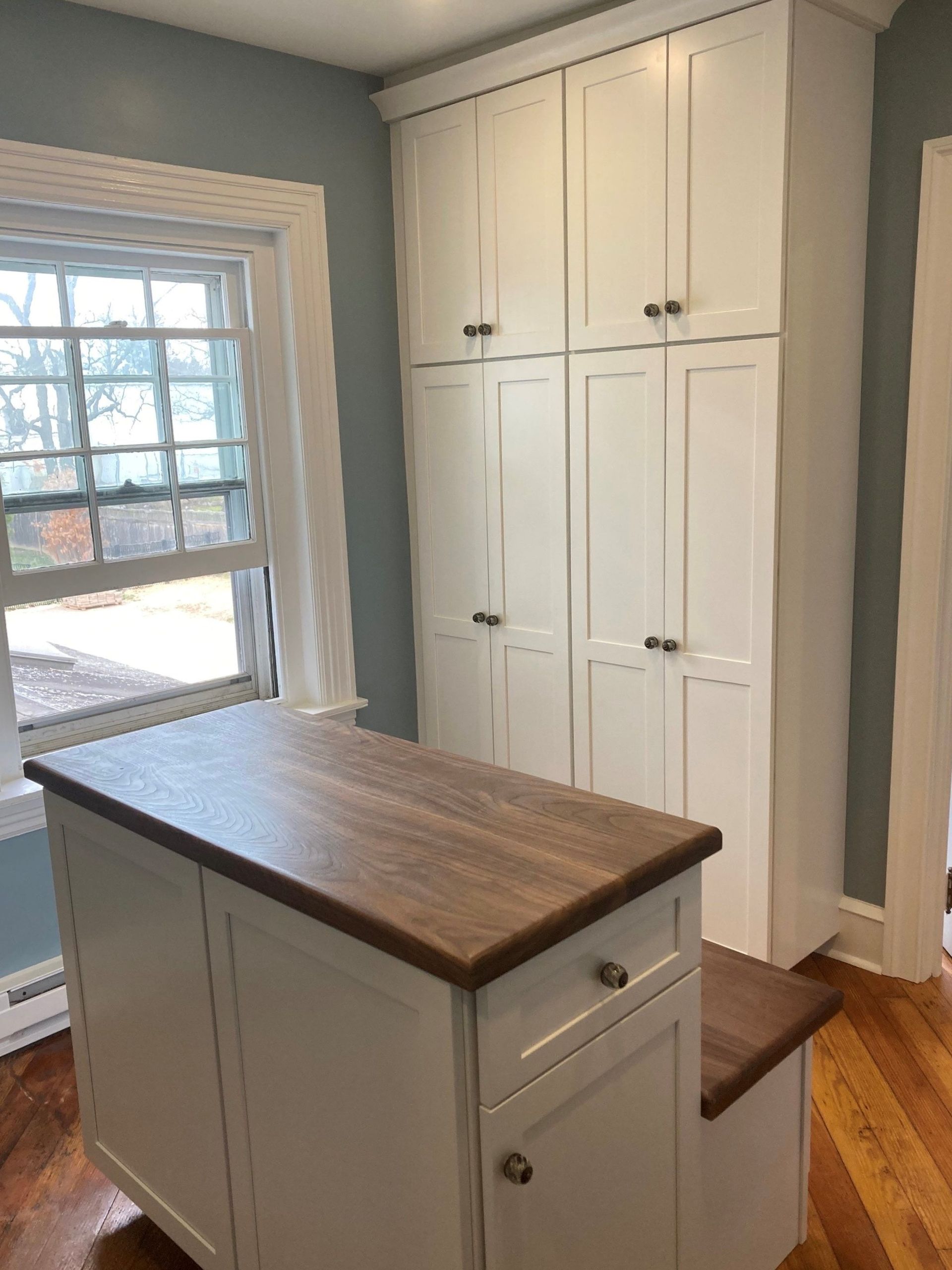 Small kitchen with white cabinets, dark wood island, and a windowed door letting in daylight.