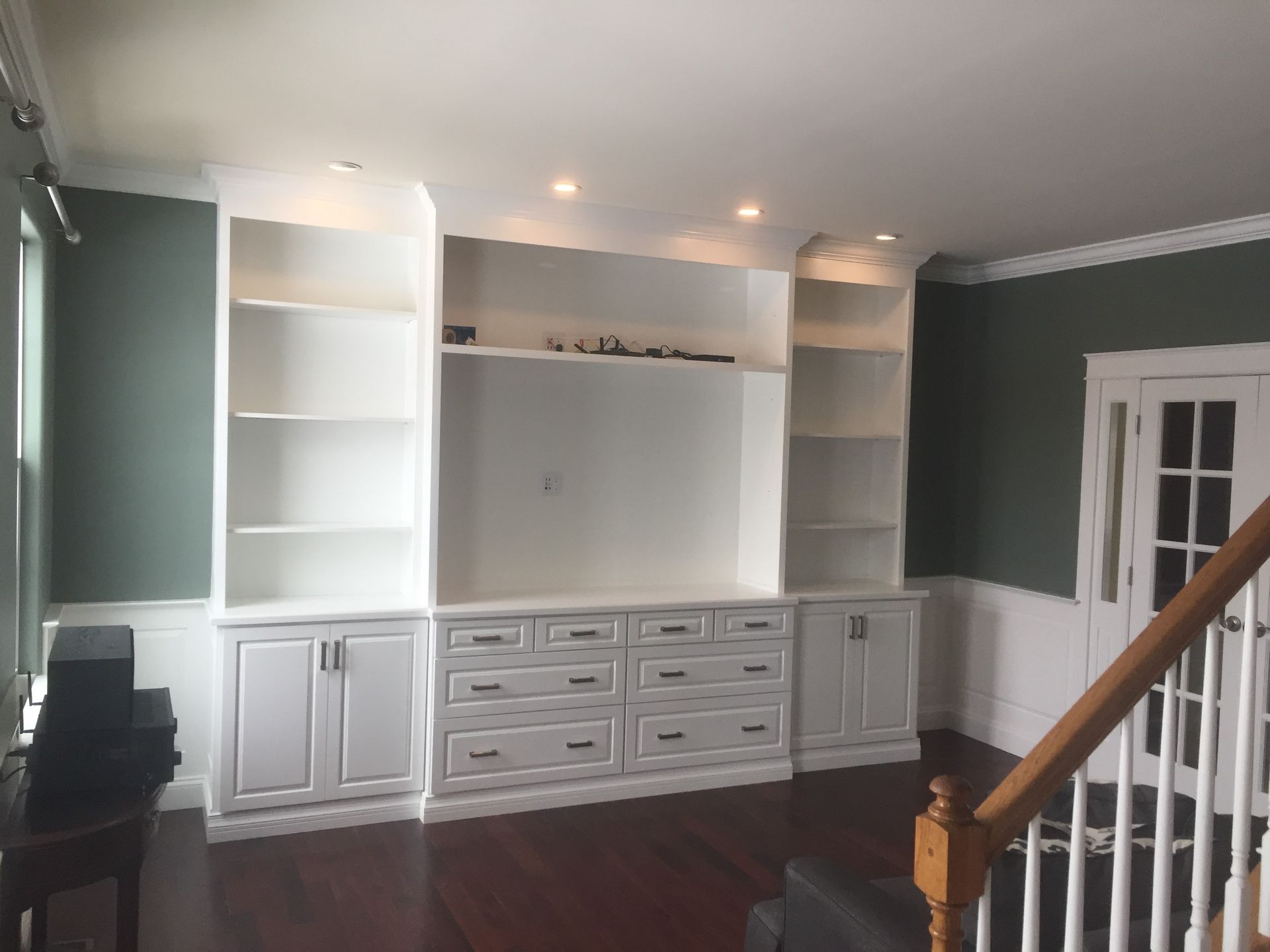 Built-in white entertainment center with shelves and cabinets against green walls in a living room.