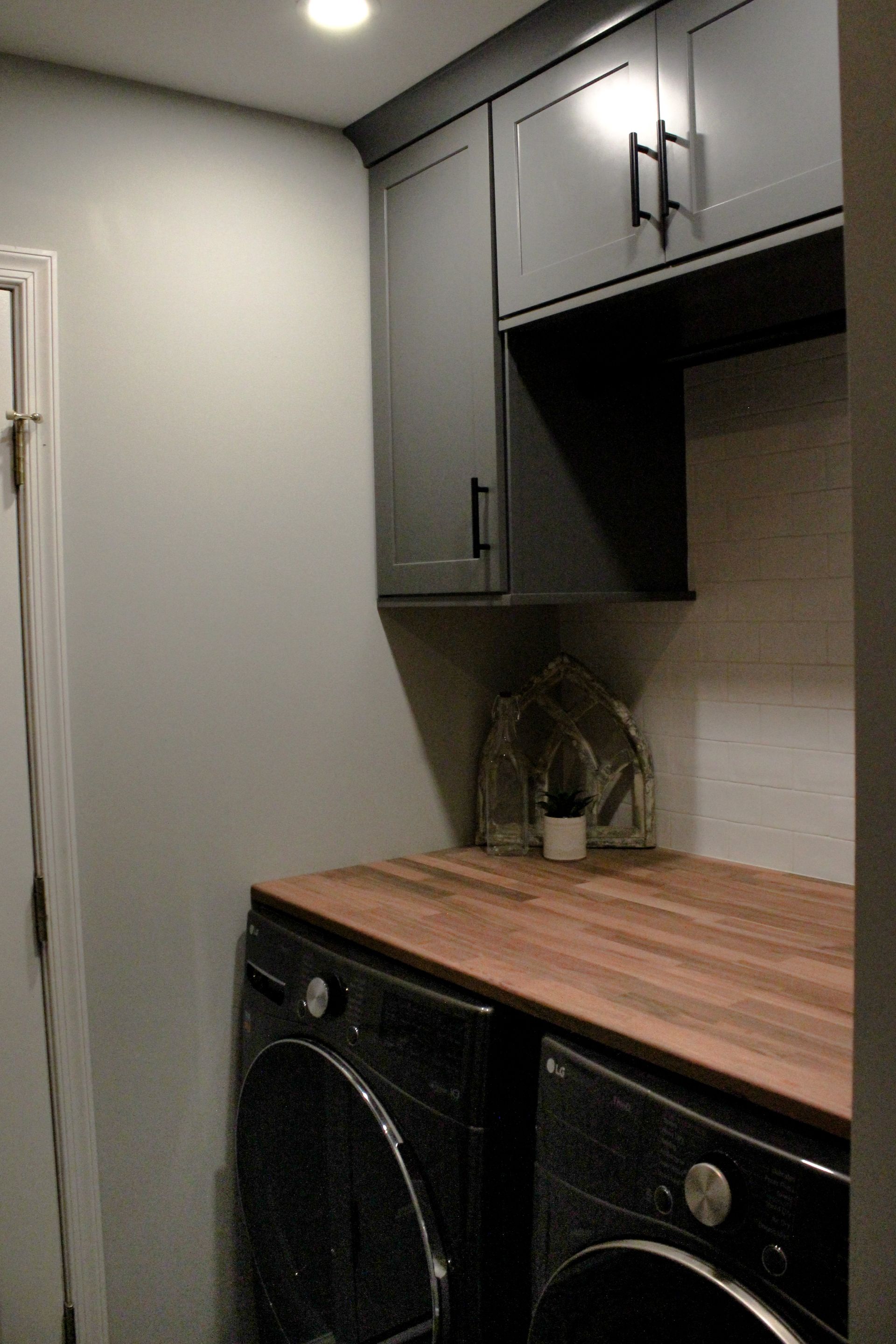 Small laundry nook with gray cabinets, wood countertop, and stacked washer and dryer.