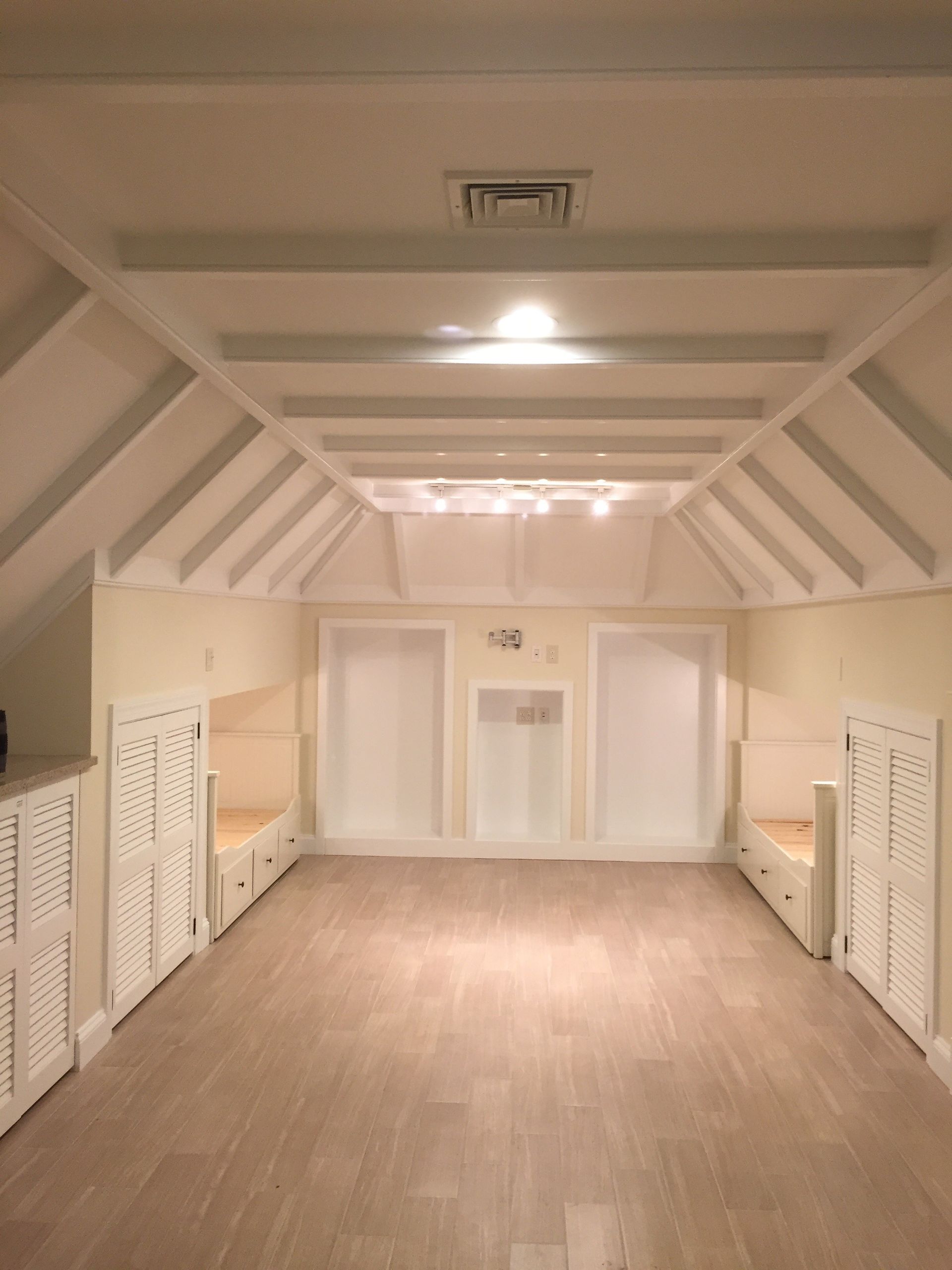 Empty white attic room with vaulted ceiling, skylight, and built-in shelves along both sides.