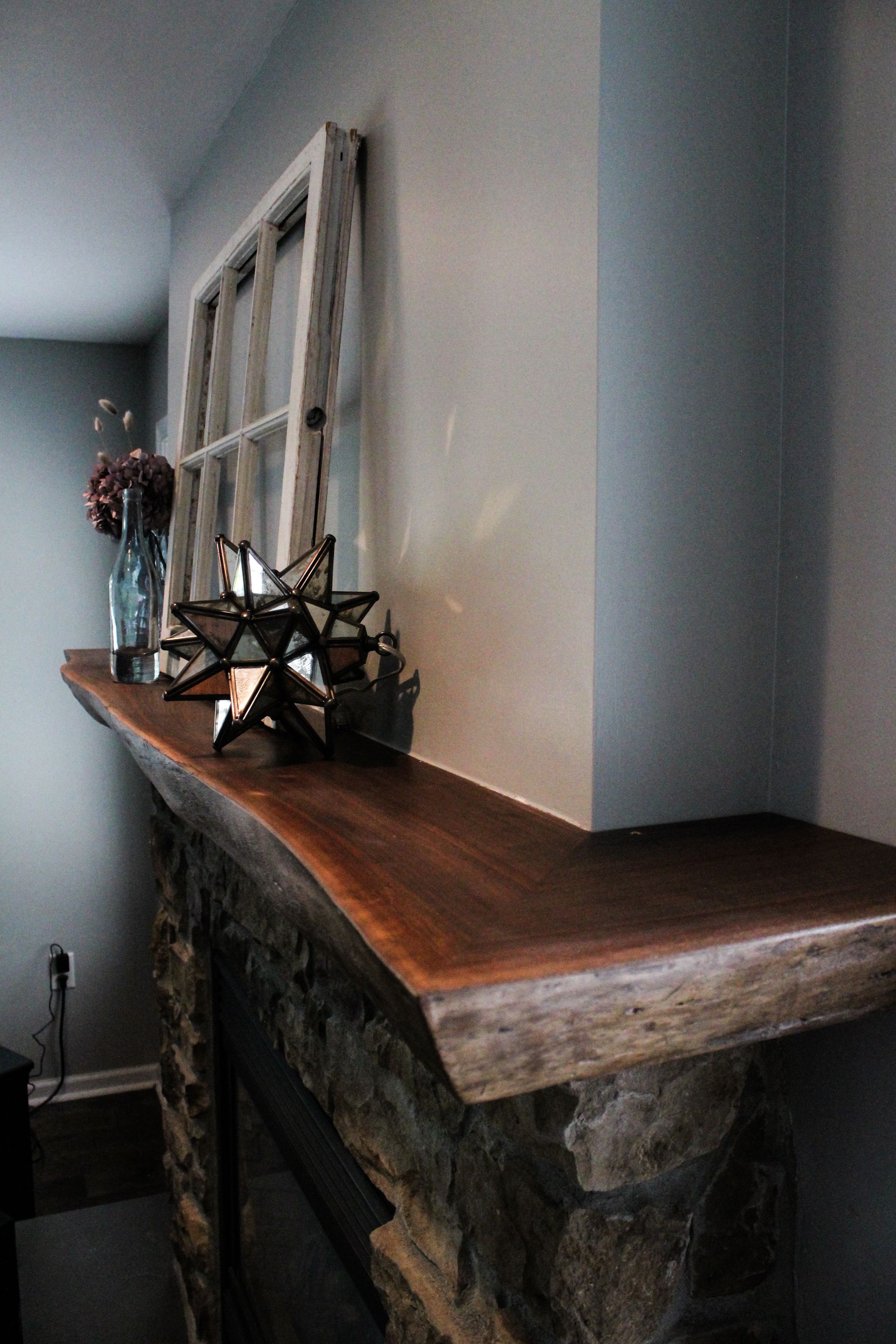 Stone fireplace mantel with wooden top, decorated with a star ornament and framed window panes against a wall.