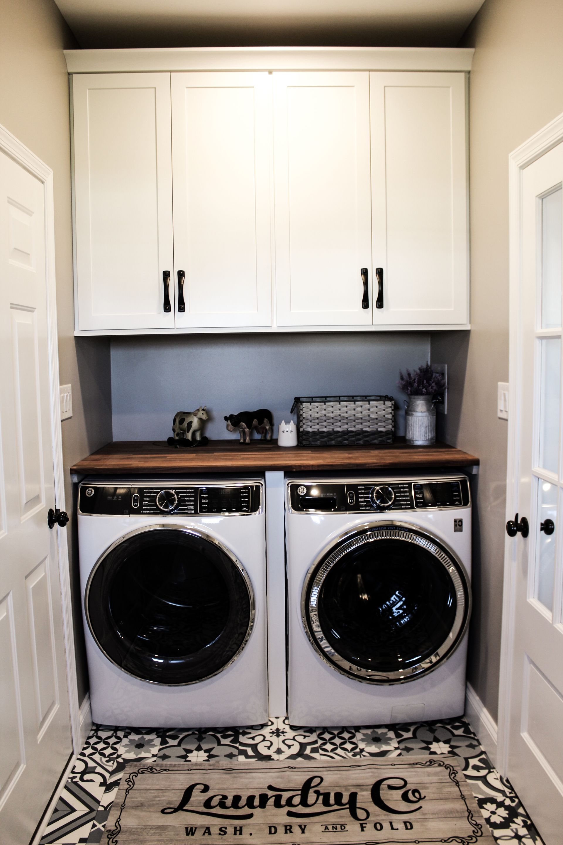 Laundry room with white cabinets, gray walls, and side-by-side washer and dryer with wooden countertop