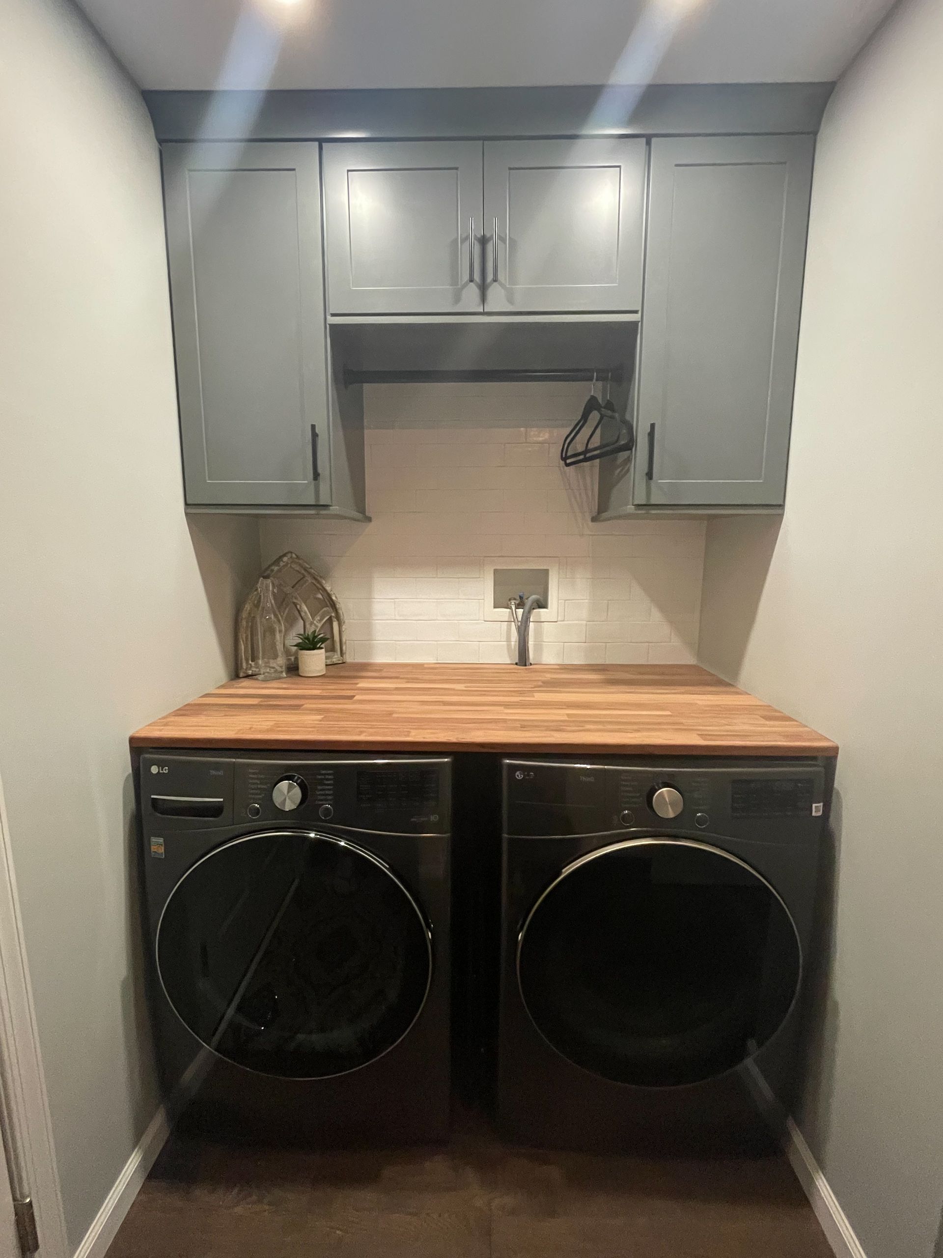 Laundry nook with gray cabinets, wood countertop, and two front-loading black appliances.
