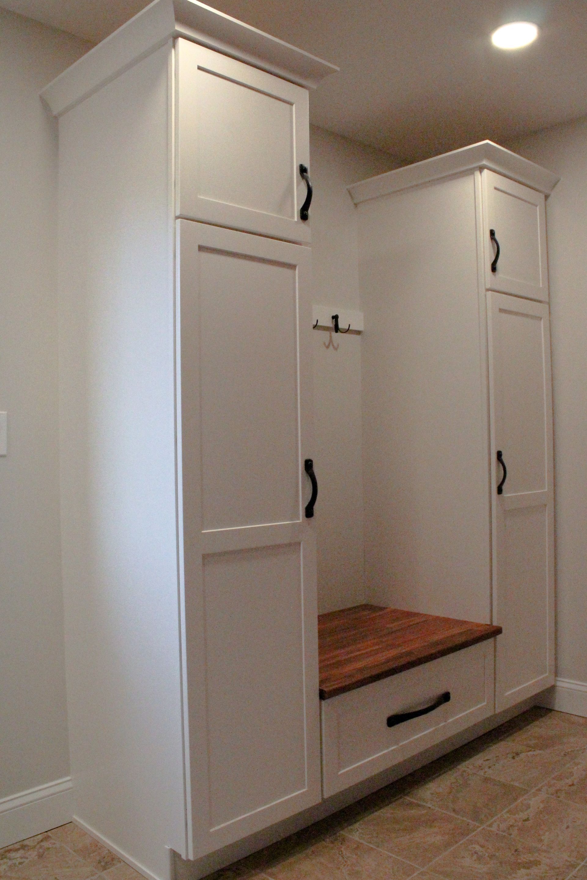 Built-in white cabinets with wood bench in a tiled hallway alcove