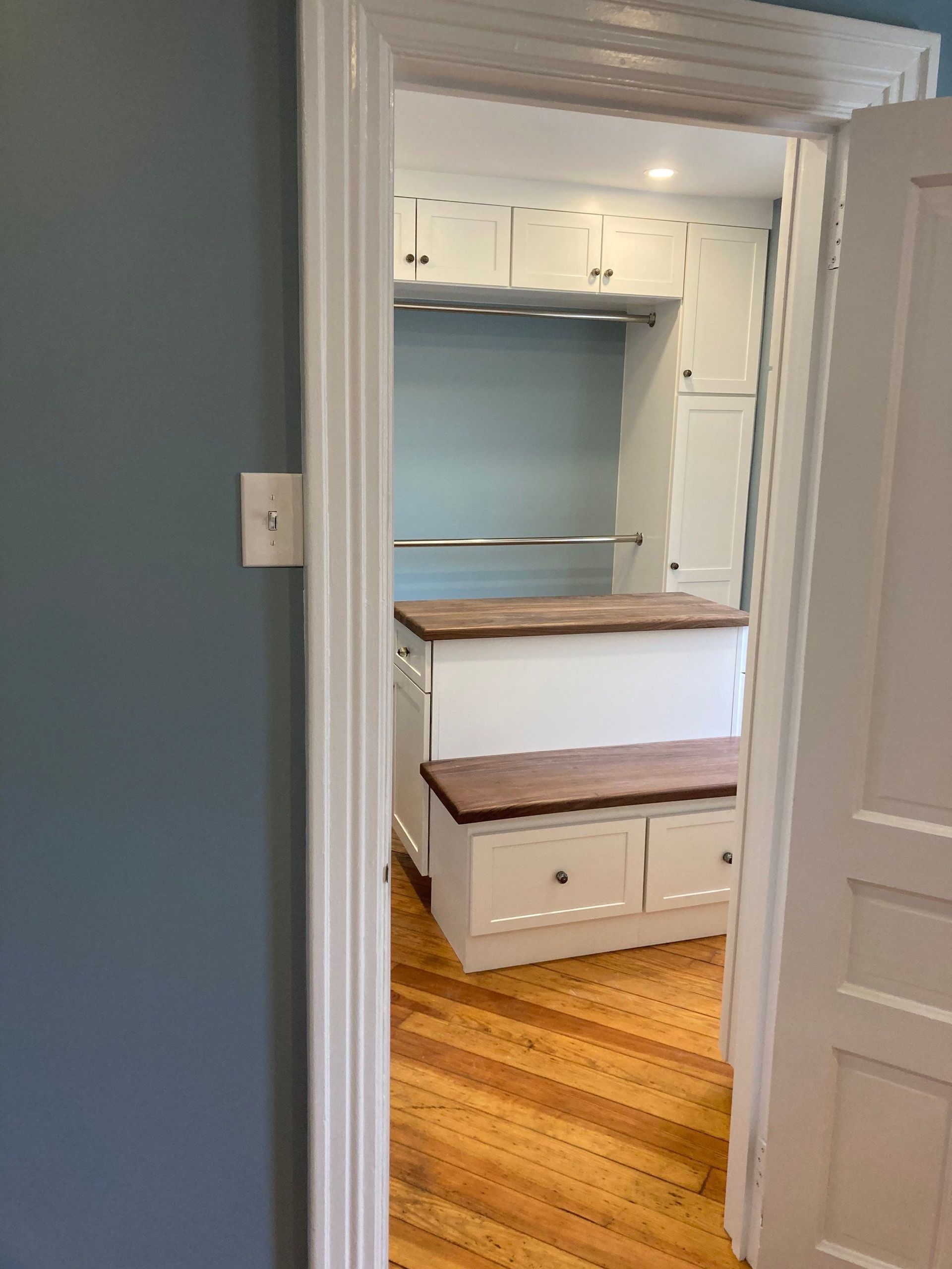 Small home office or nook with built-in desk, white cabinets, and blue walls seen through a doorway