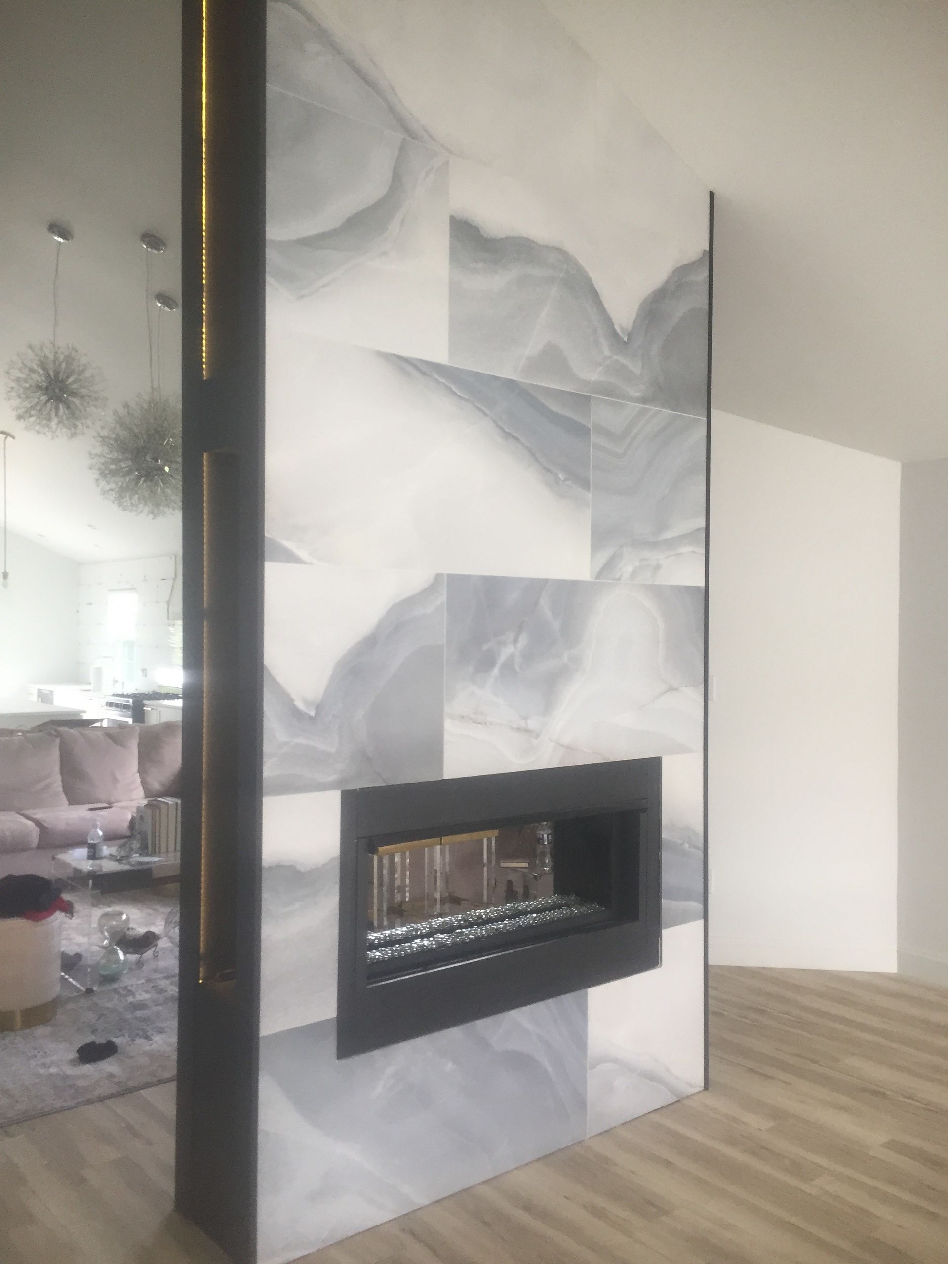 Modern living room with a marble-patterned fireplace wall and open gas fireplace, wood flooring, and a sofa in the background