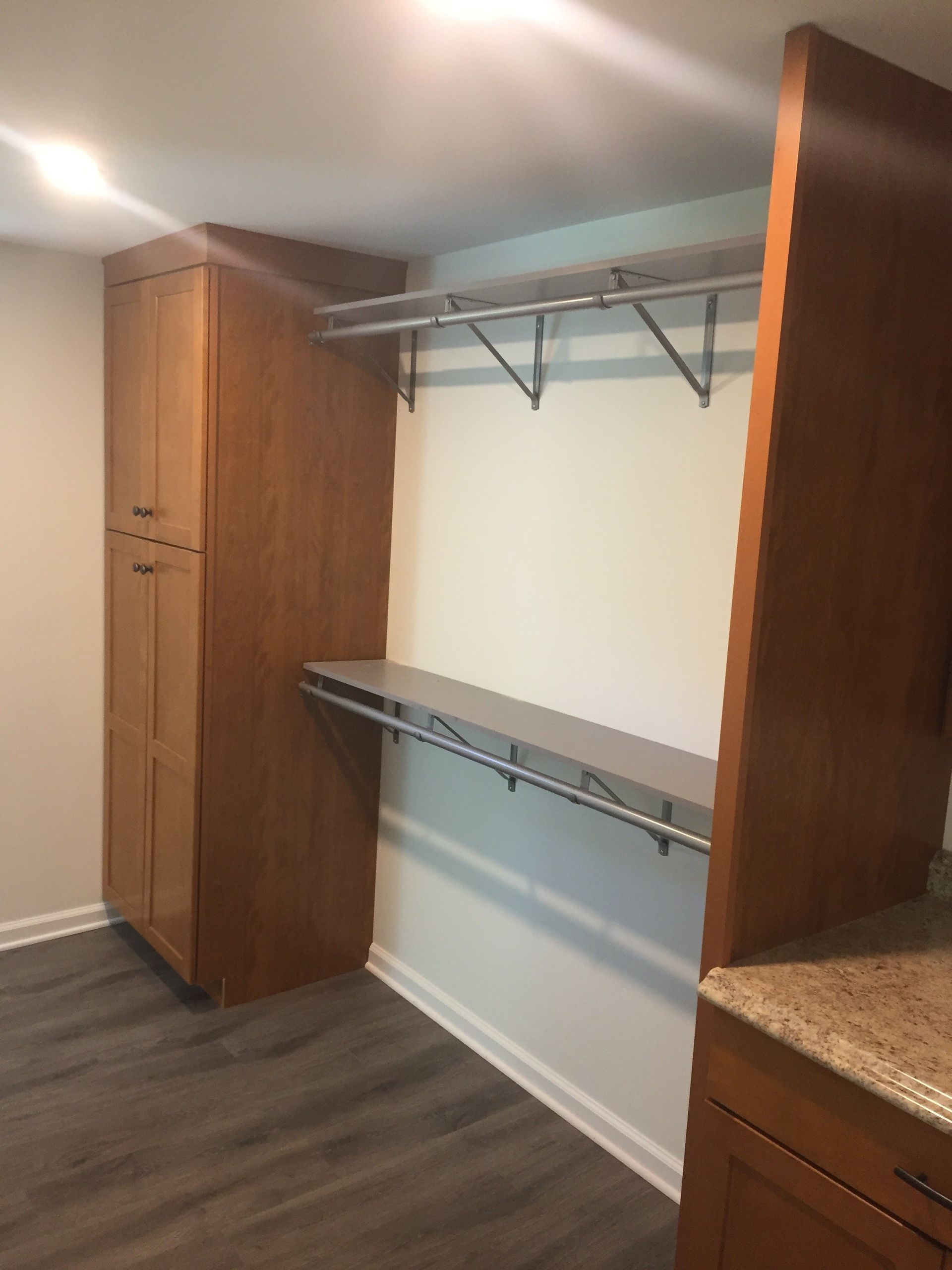 Walk-in closet with wood shelving, wire hanging rods, and dark wood cabinets on a gray floor.