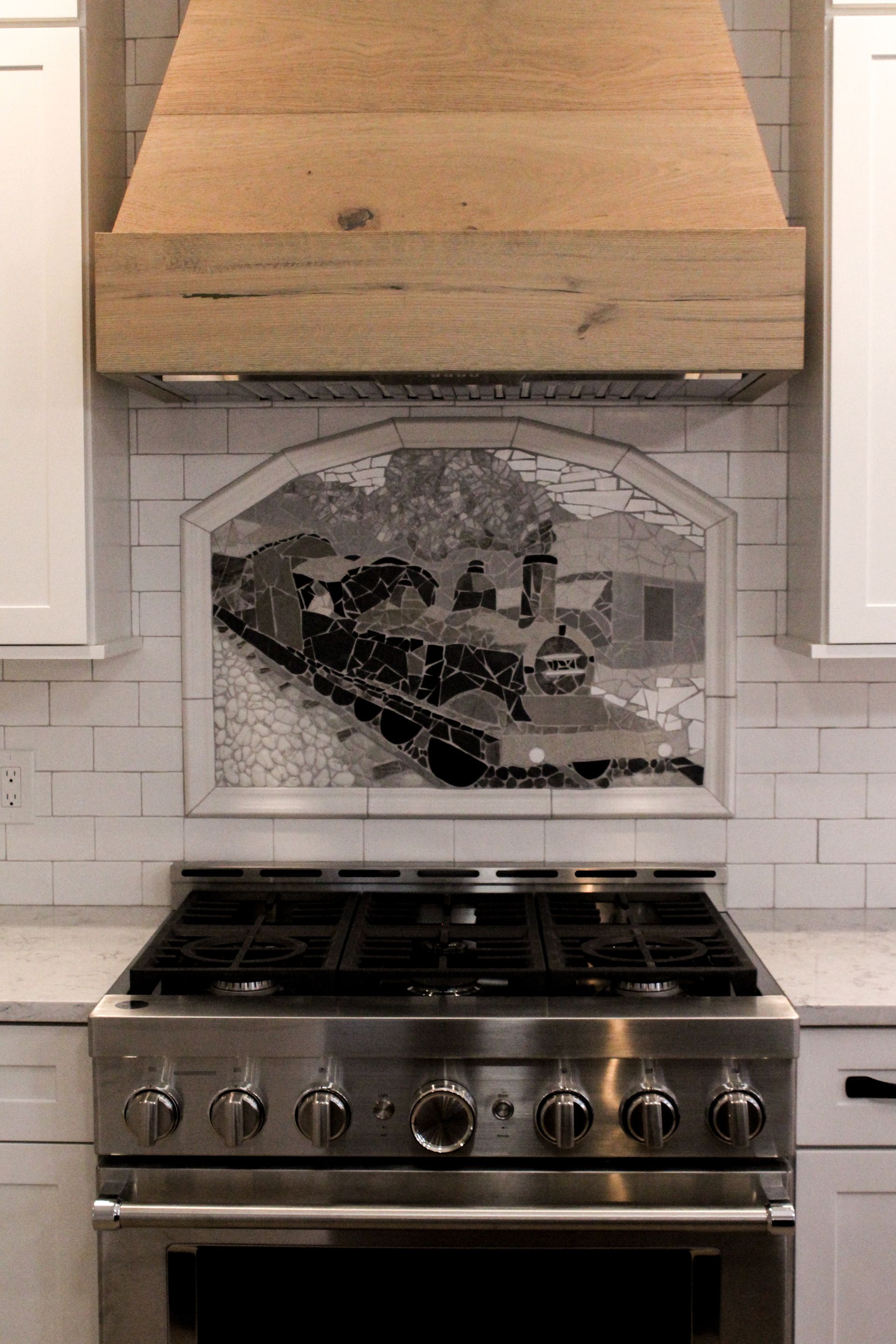 Kitchen stove with stainless steel range and tile backsplash featuring a black-and-white mural