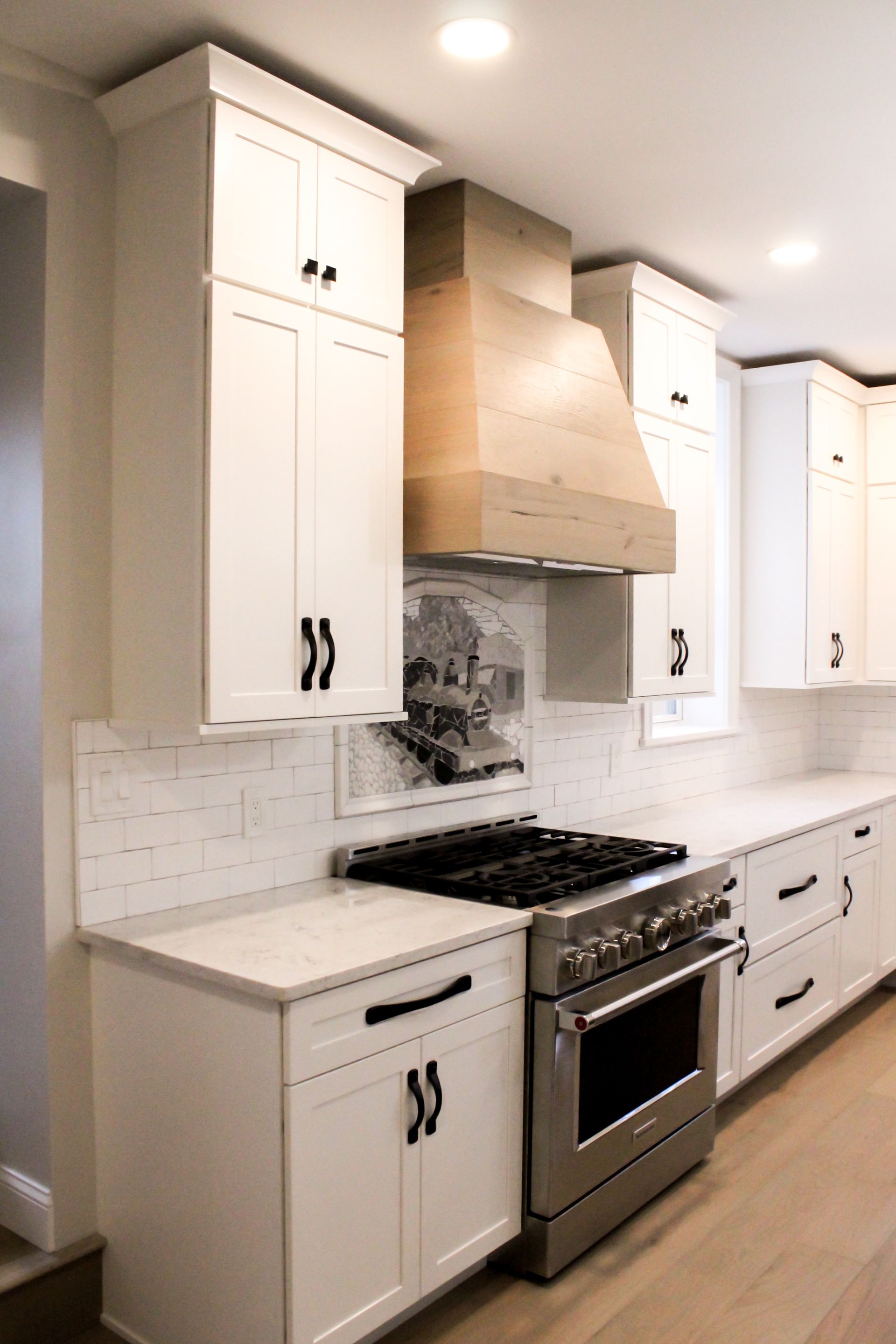 Bright white kitchen with stainless steel stove and hood, white cabinets, and light wood floors