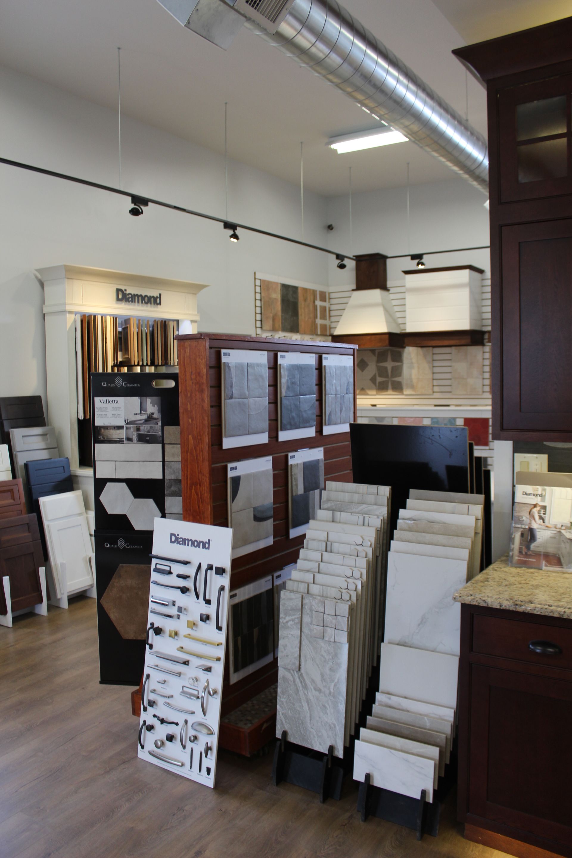 Tile showroom with samples, display racks, and cabinets under bright overhead lighting