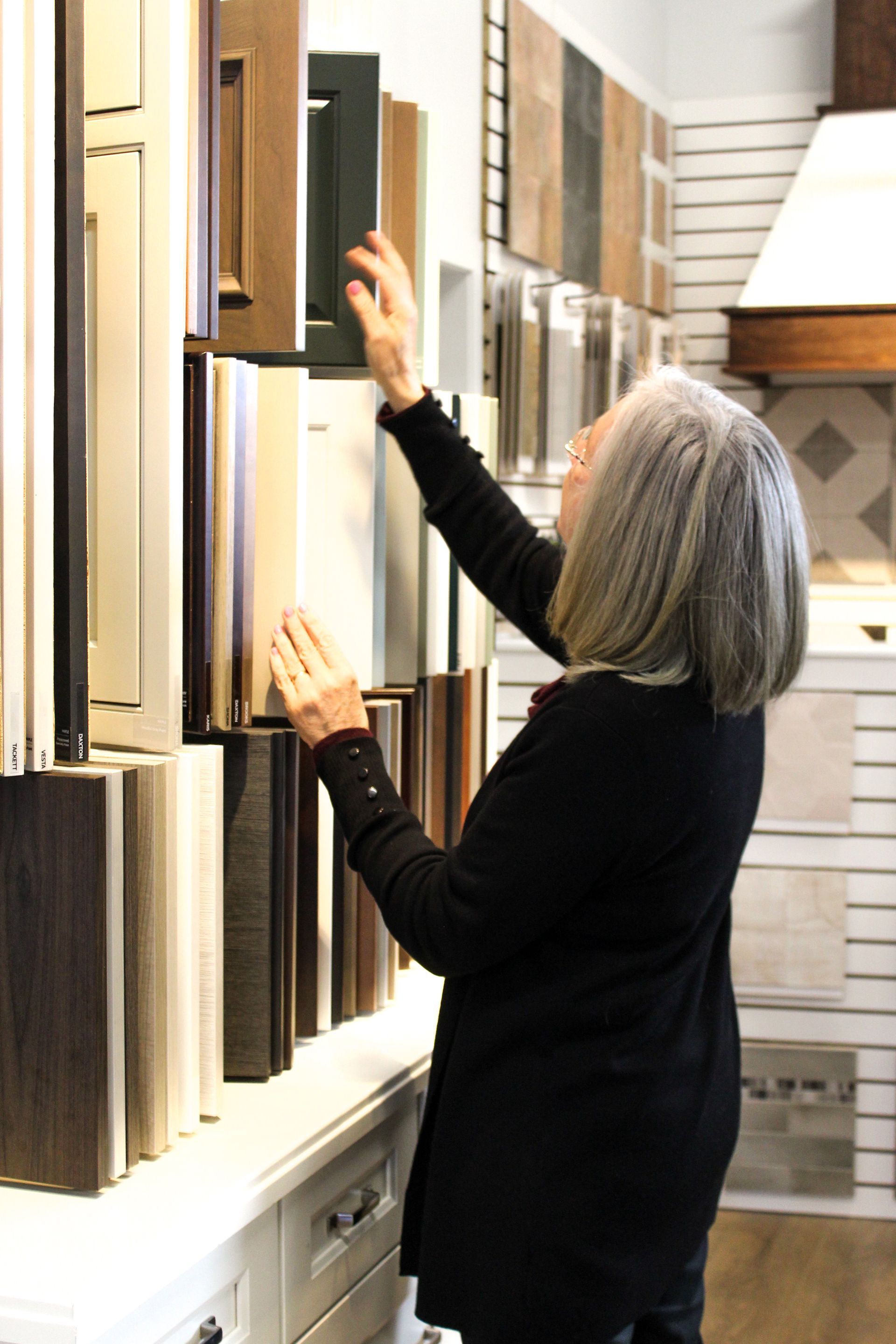 Woman in black sweater reaching for wood sample boards in a showroom