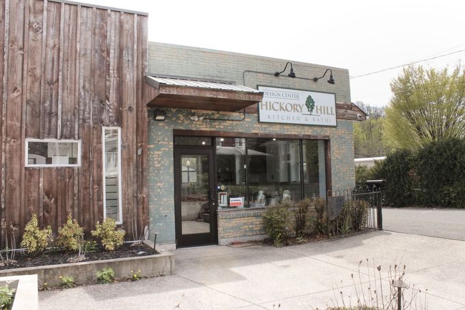 Small storefront with wood siding, glass entrance, and a white sign beside a paved parking area.