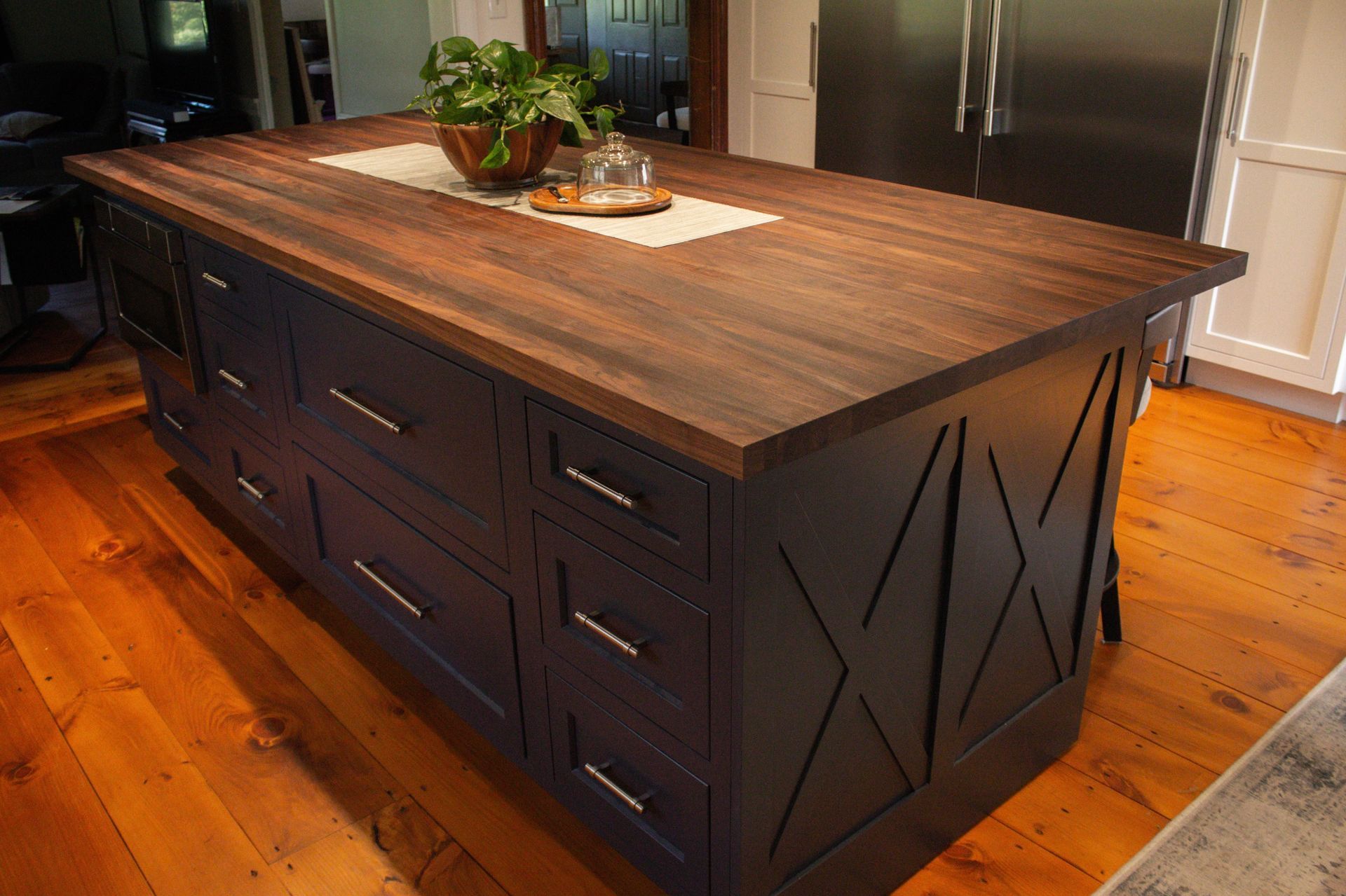 Large dark kitchen island with wood countertop and built-in drawers in a bright kitchen.