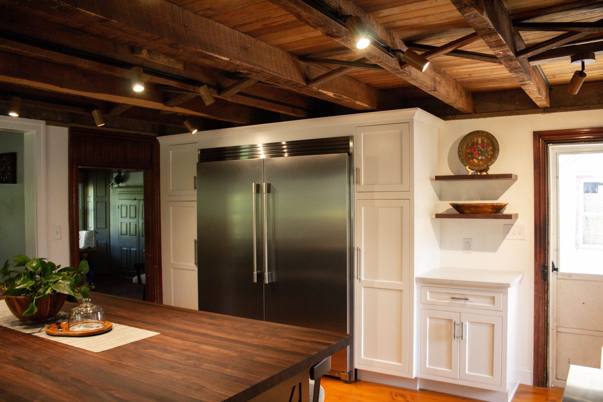 Modern kitchen with stainless steel fridge, wood island, white cabinets, and exposed ceiling beams