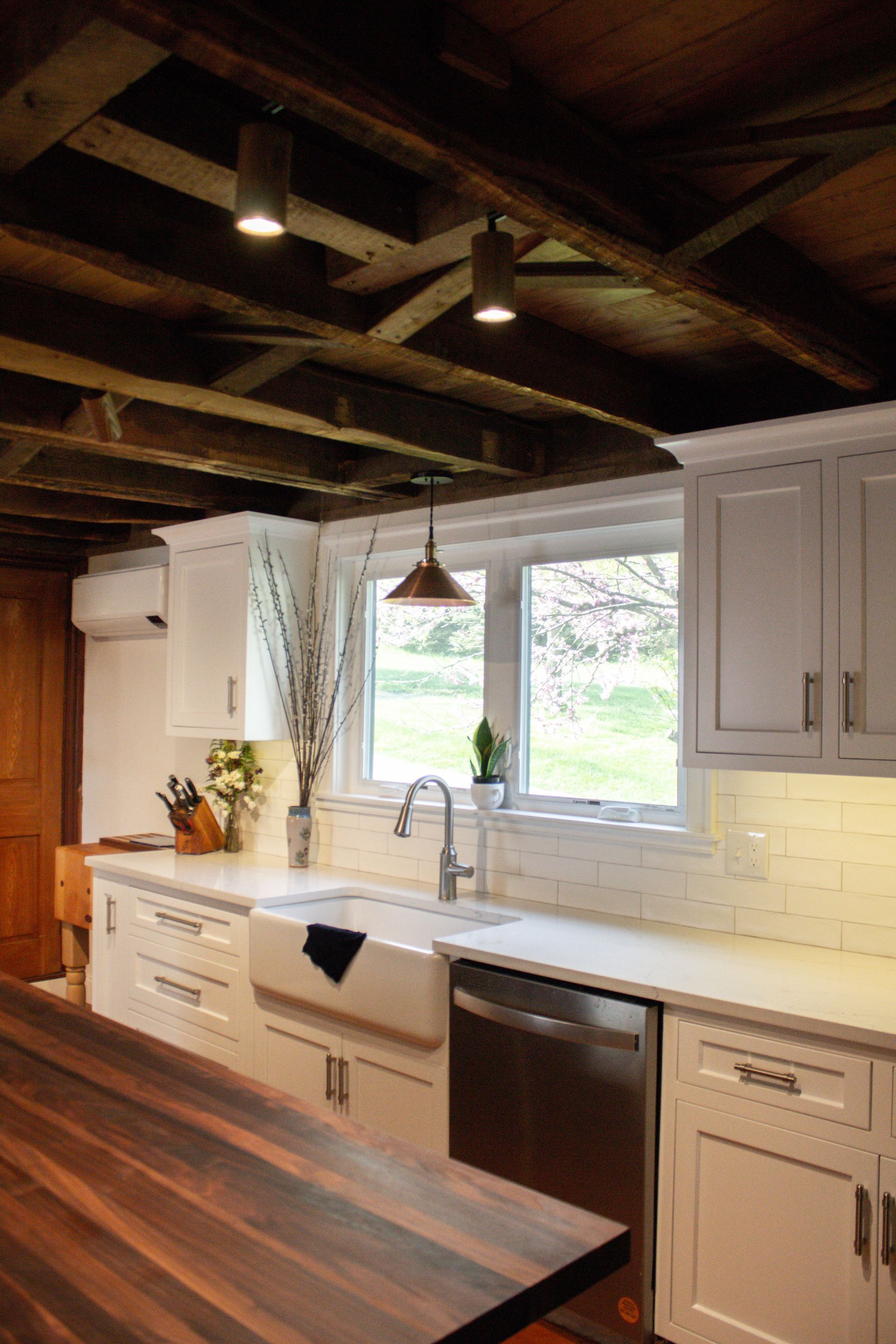 Modern kitchen with white cabinets, farmhouse sink, wood island, and exposed ceiling beams