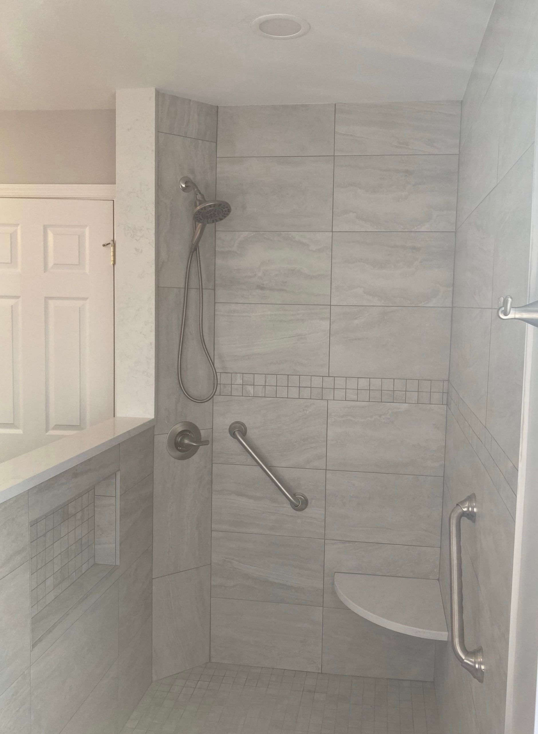 Accessible shower stall with grab bars, fold-down seat, and handheld showerhead in a tiled bathroom