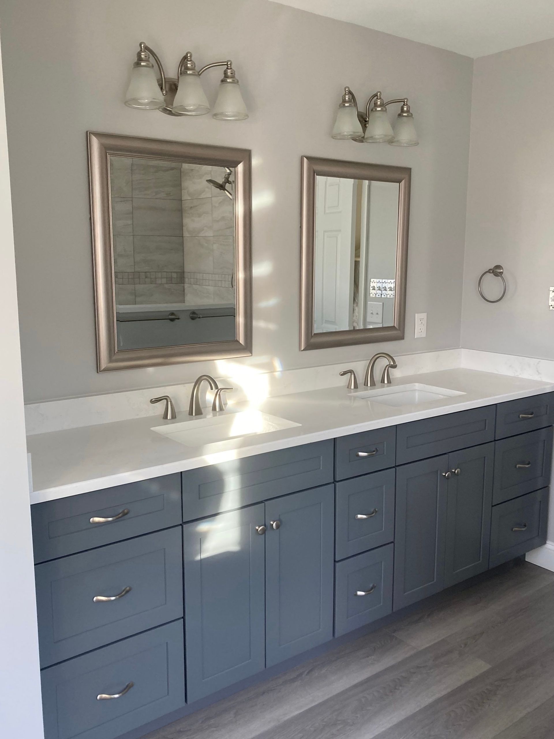 Modern bathroom with double vanity, blue cabinets, white countertops, and two mirrors.