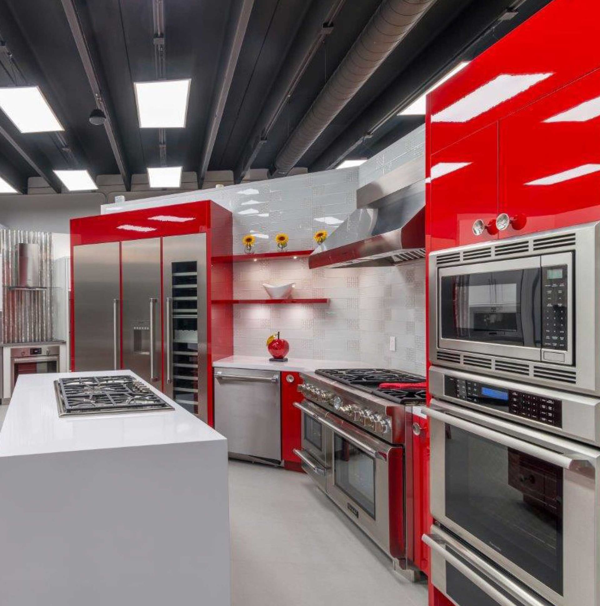 Modern kitchen showroom with glossy red cabinets, stainless steel appliances, and white countertops