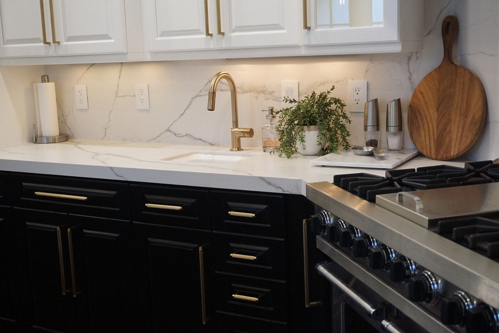 A kitchen with black cabinets , a stove , a sink , and a wooden cutting board.