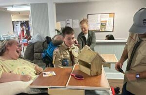 A boy scout and resident Kim are at a table building a birdhouse. 