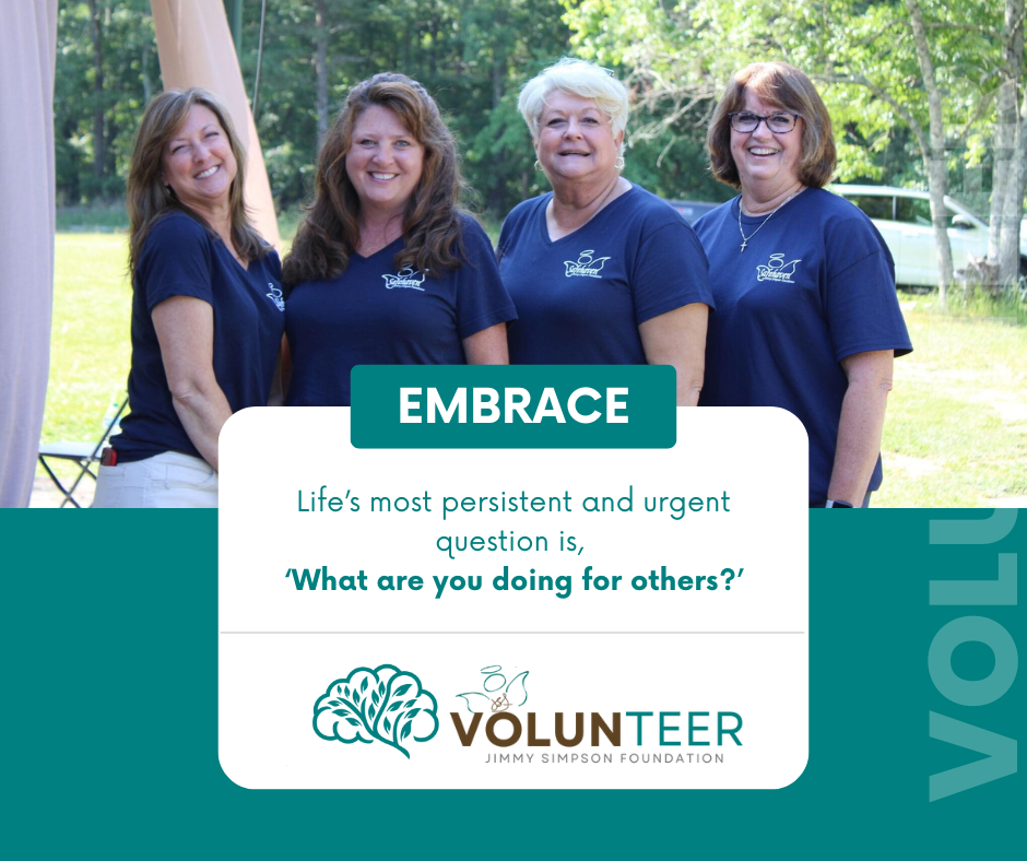 Four smiling people in matching navy blue t-shirts stand outdoors, overlaid with a quote about helping others.