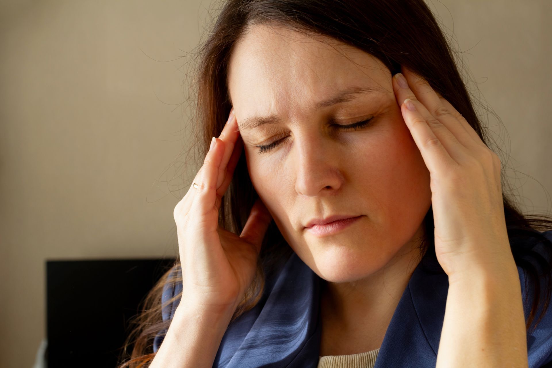 Woman pressing her temples with eyes closed, appearing to have a headache or stress