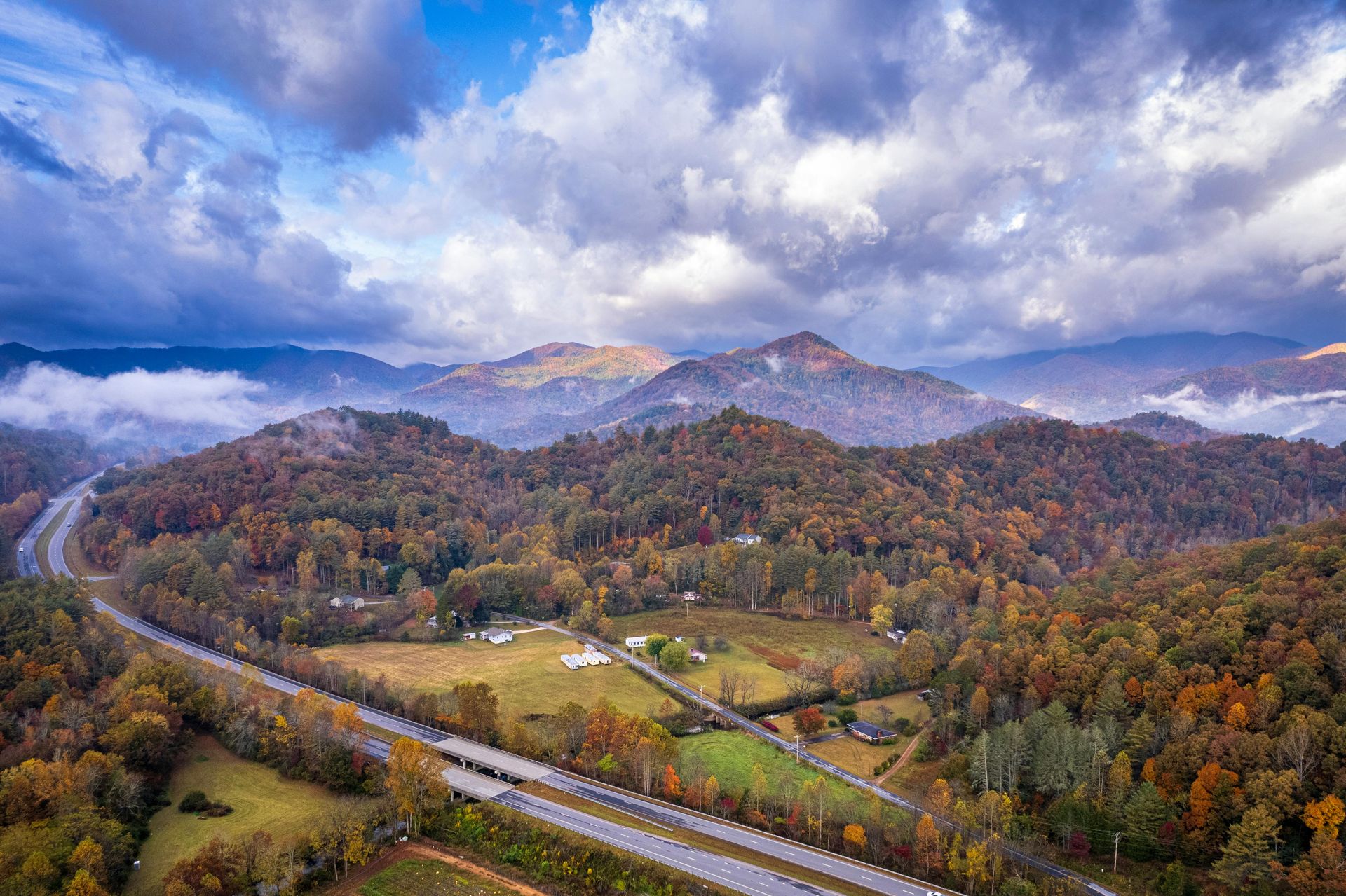 Autumn mountains and forest under dramatic cloudy sky, with a winding road in the foreground